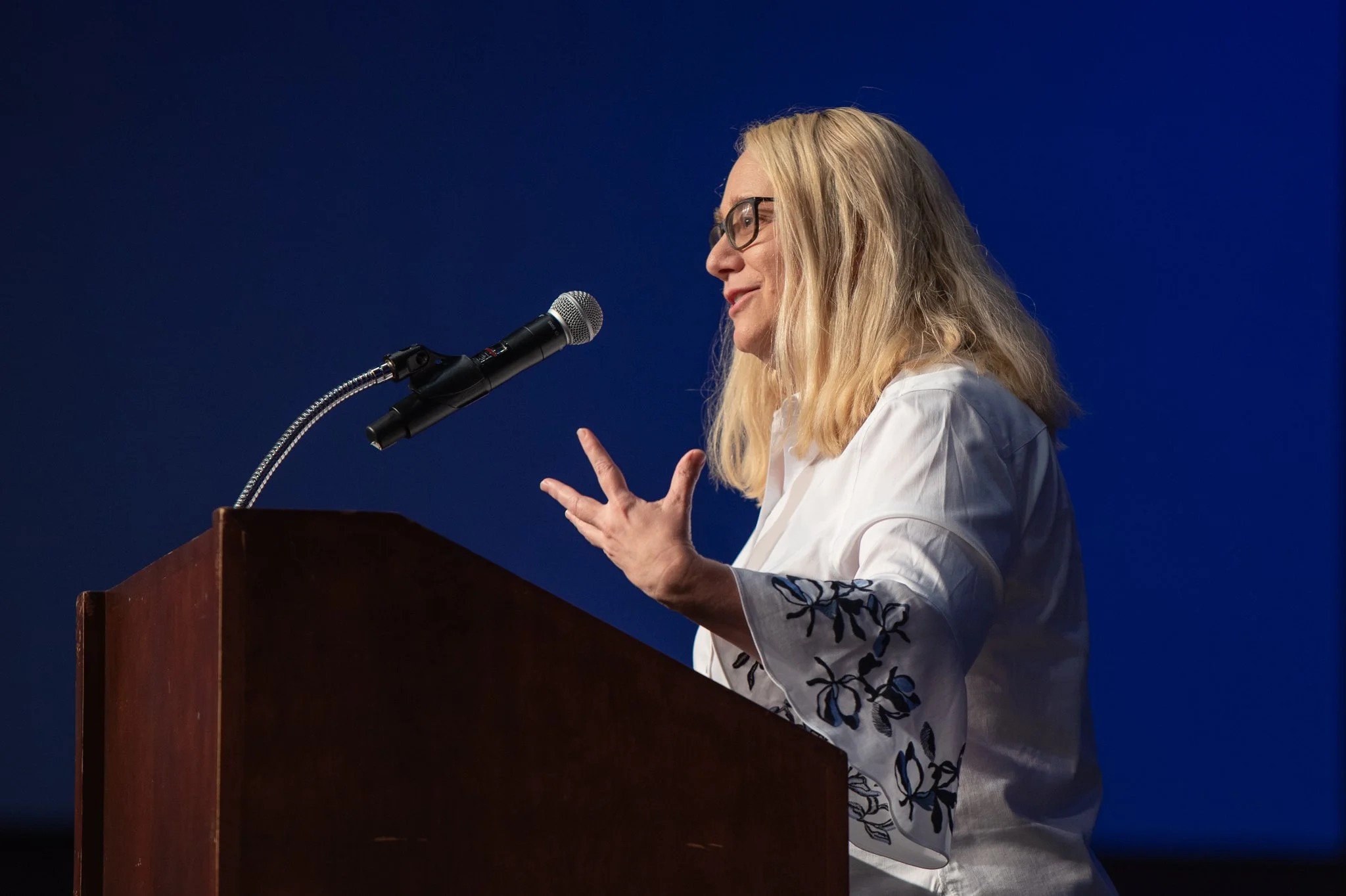 Dreama Denver speaking at a podium with a microphone, delivering a presentation to an audience at a professional event.