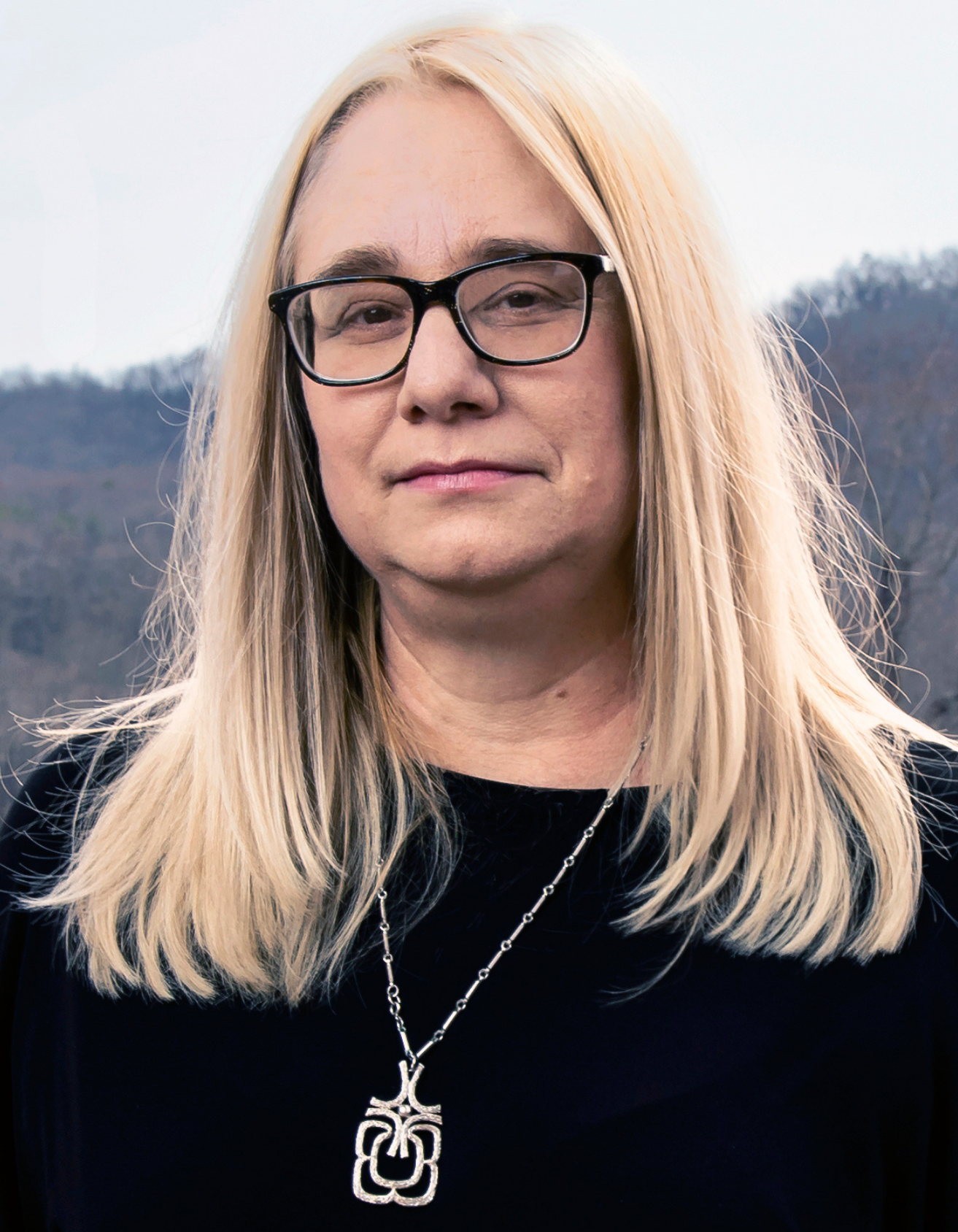 Dreama, speaker, author, and thought leader, smiling outdoors with rolling hills in the background.