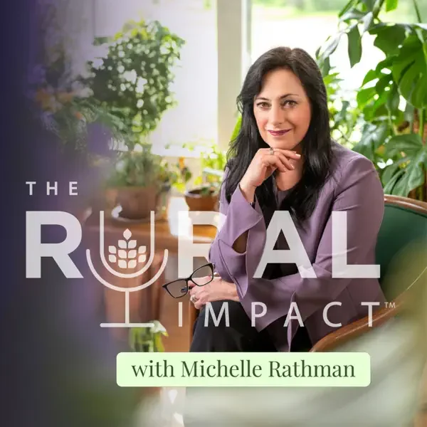 A woman with dark hair smiling while sitting in a room with plants, wearing a light purple jacket, with the words 'The Rural Impact with Michelle Rathman' overlayed on the image.