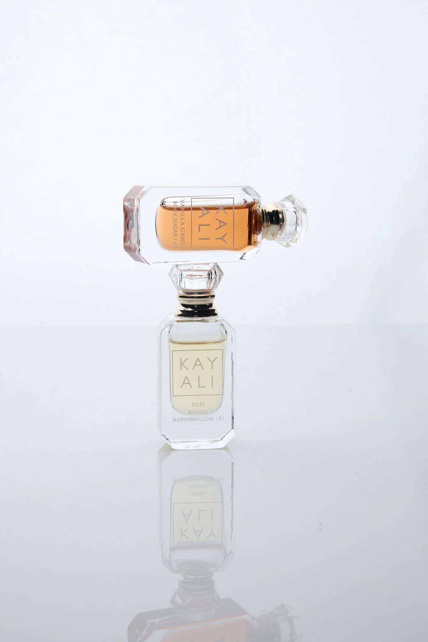 A clear glass perfume bottle with a rectangular shape and a large, faceted cap. The bottle contains a light amber-colored liquid and features labels with the text 'KAYALI' and 'VANILLA CANDY'.