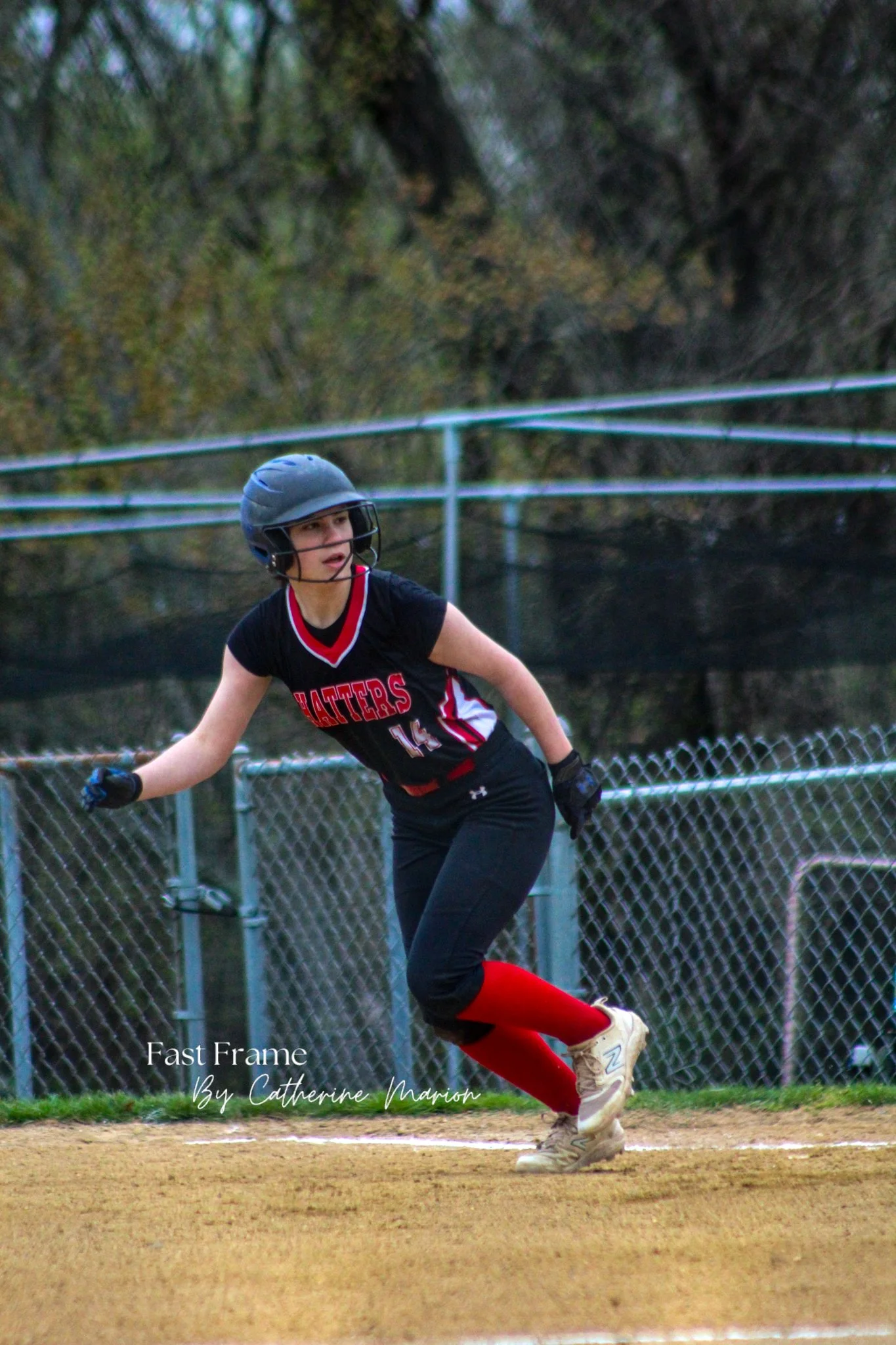 A female softball player wearing a helmet and a black and red uniform, running on a baseball or softball field.