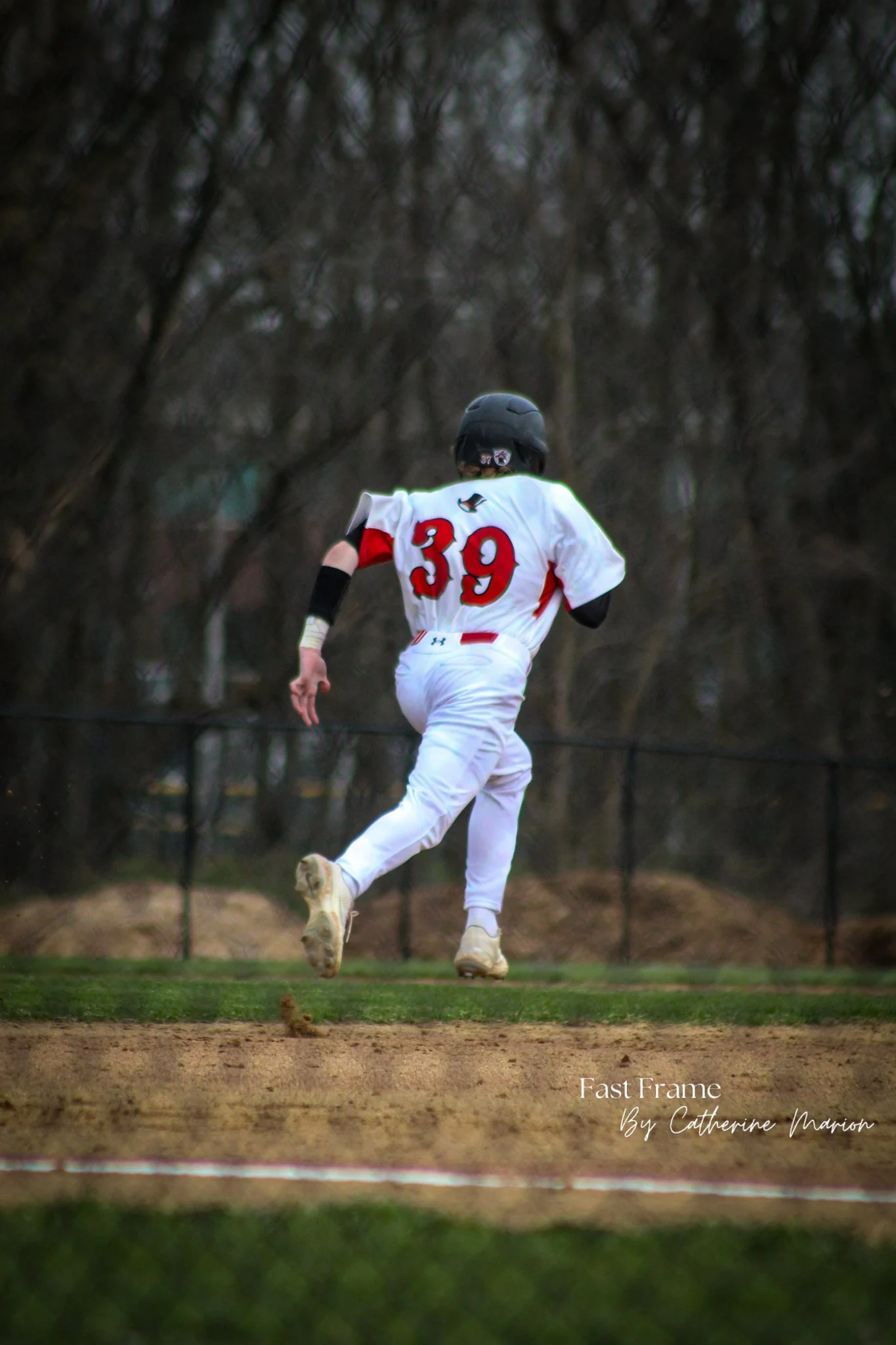 A baseball player wearing a black helmet and jersey with the number 39 on the back, running on a dirt field during a game, with a dark, trees-filled background.