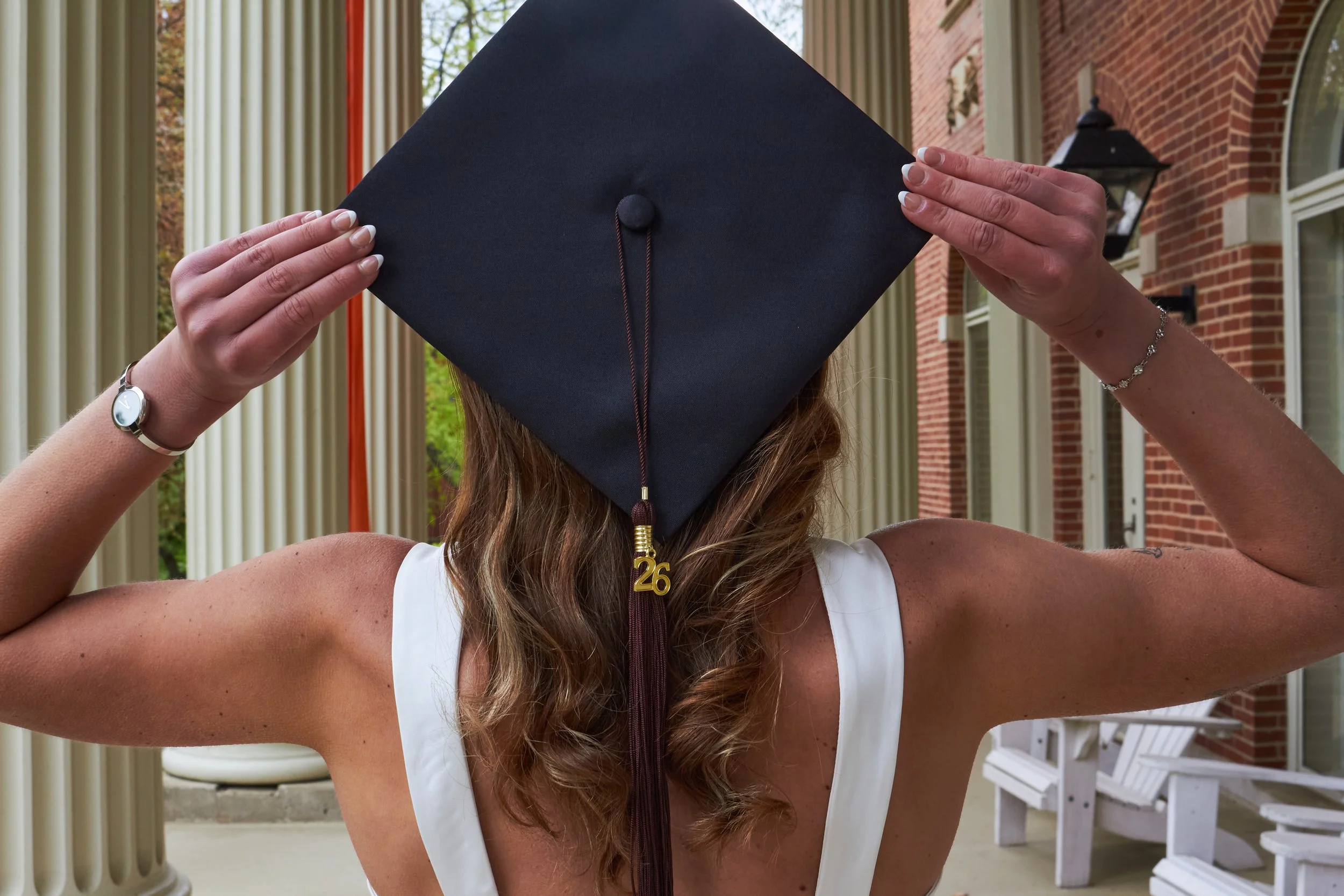Person holding a graduation cap over their head, showing a gold '26' necklace.