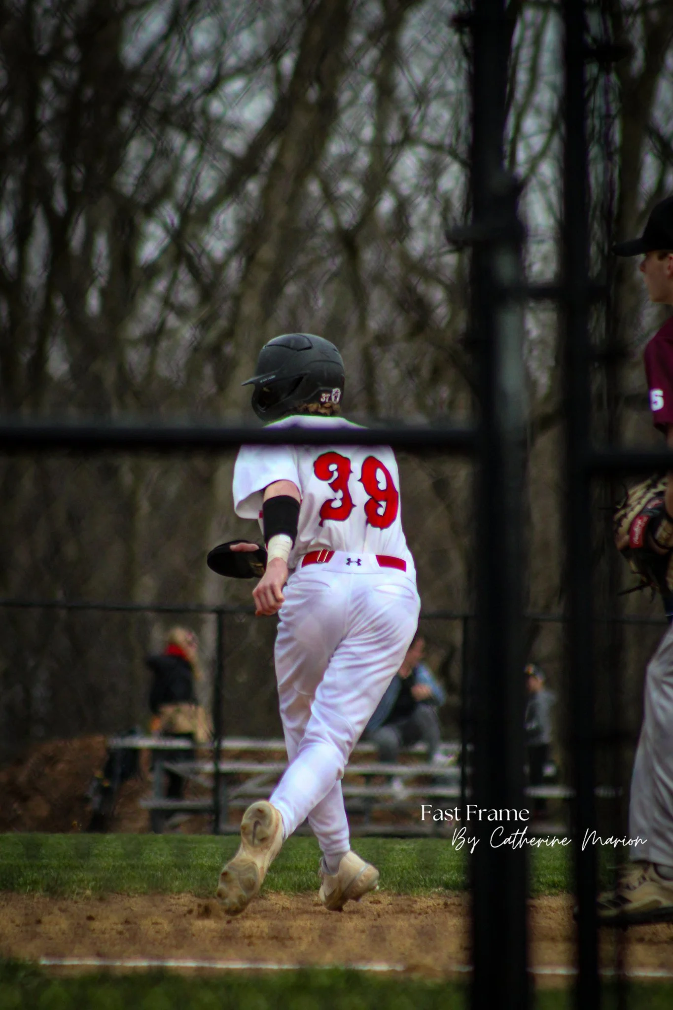 A baseball player wearing a black helmet and white uniform with the number 39 on the back, running on the field. The image is taken from behind, showing the player's back and part of the field. Surrounding trees are blurred in the background.