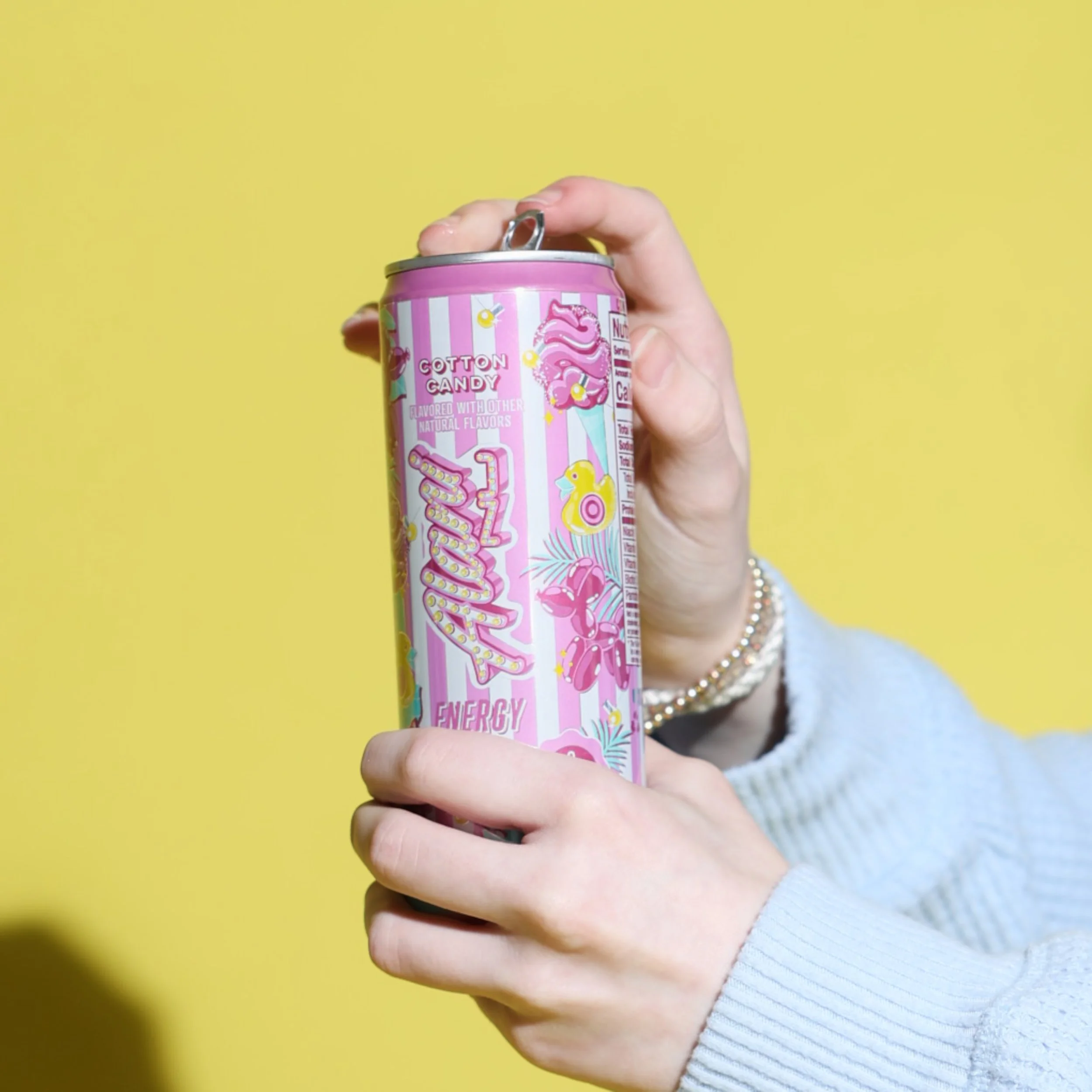 Person opening a pink can labeled "Cotton Candy" against a yellow background.
