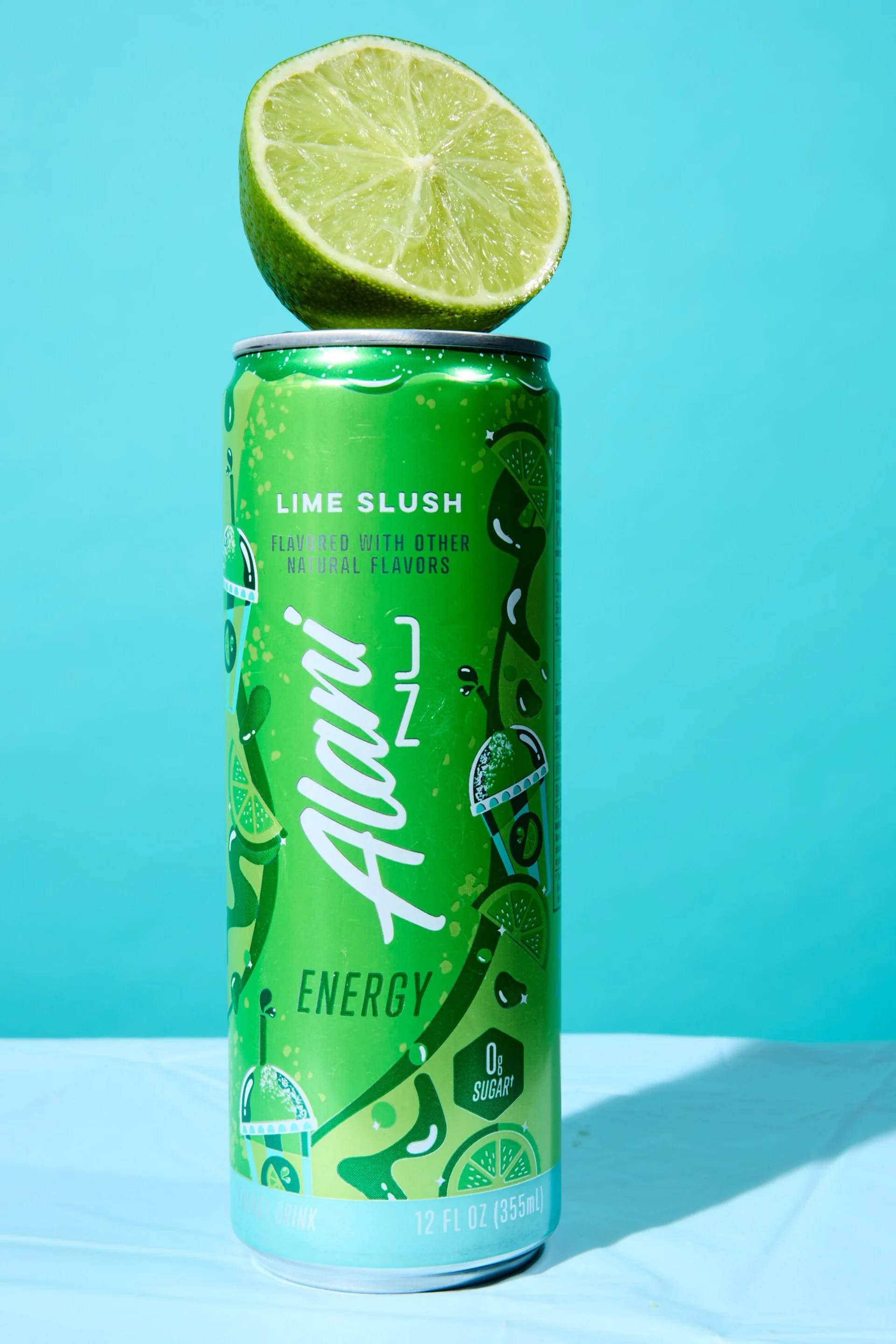A can of soda with a half lime on top, set against a light blue background.