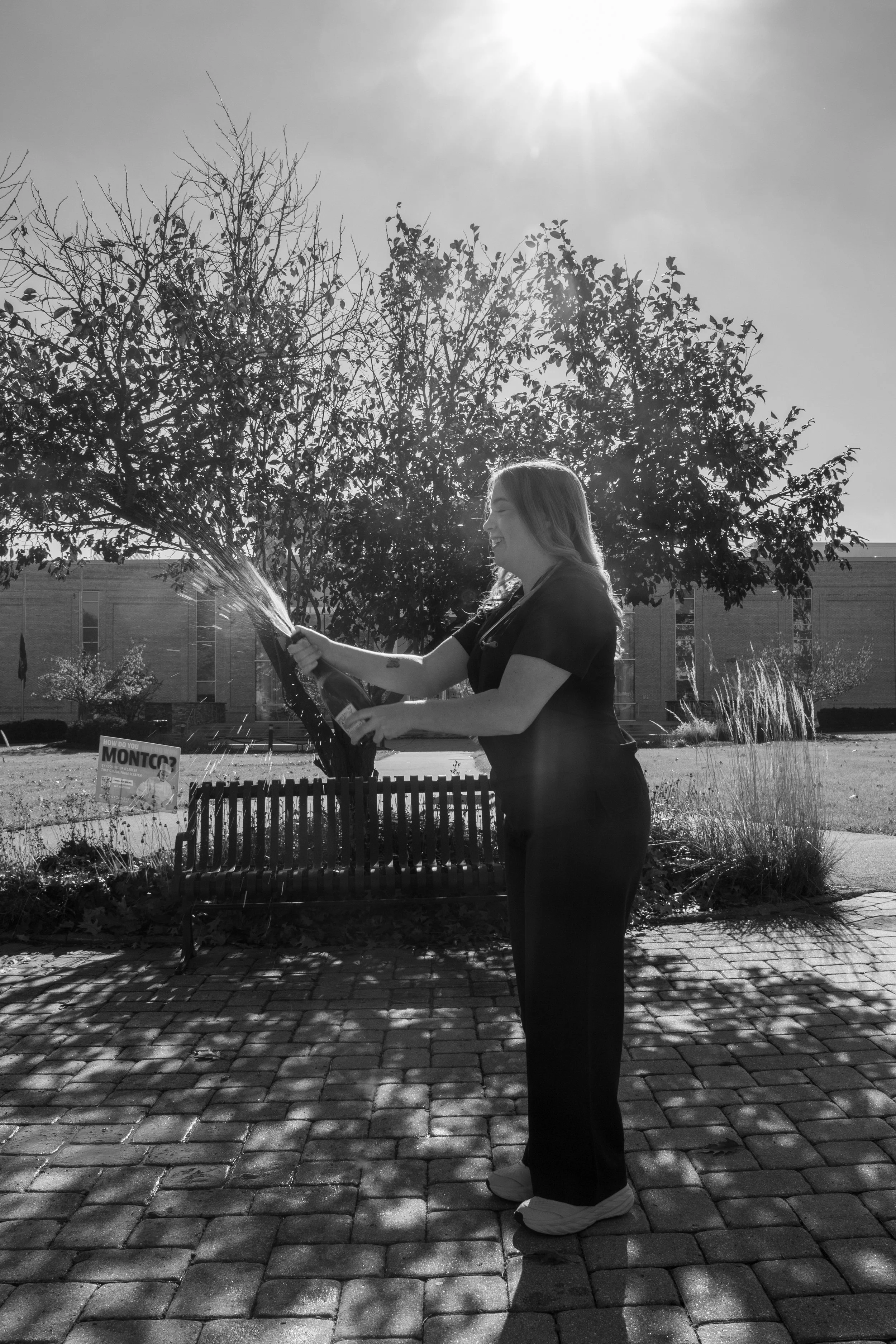 A woman in medical scrubs watering a tree outdoors.