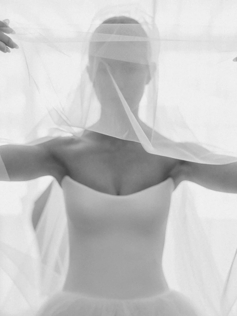 A client of Rachel Lusk Hair and Makeup, a Bridal Hair & Makeup Artist in Napa Valley, offering destination bridal hair & makeup, is holding a transparent fabric or sheet in front of her face, creating a layered and shadowed effect.