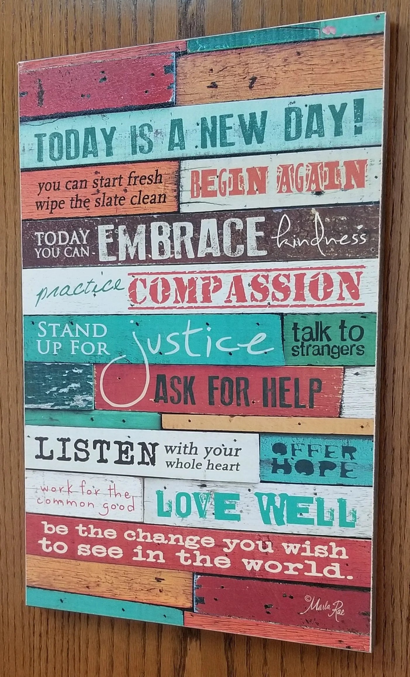 Colorful wooden sign with inspirational quotes about kindness, compassion, justice, and love, featuring a variety of fonts and handwritten styles.