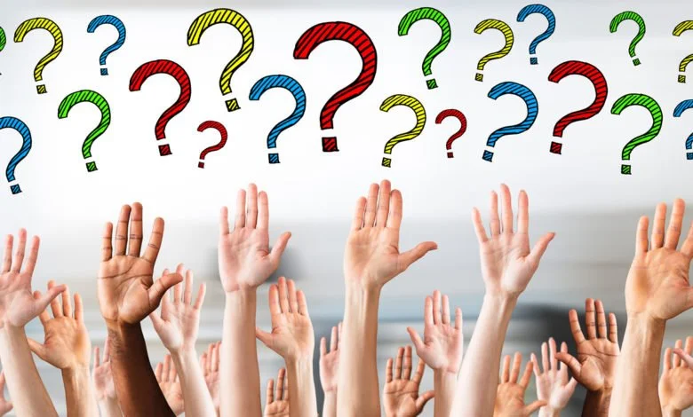 Multiple raised hands of diverse skin tones with colorful question marks in the background.