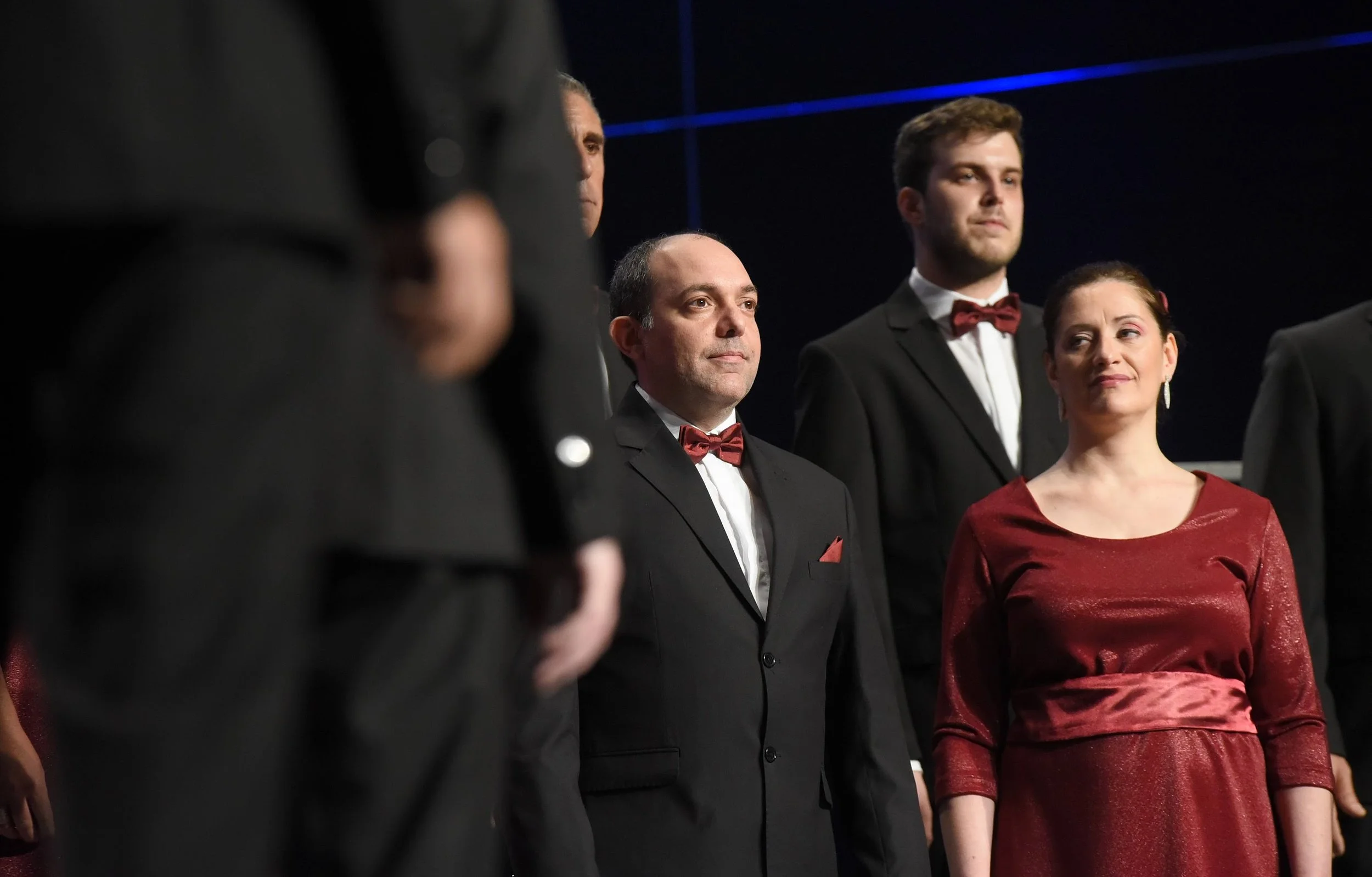 Grupo de personas vestidas con traje formal en un escenario, algunas con corbatas de moño, en lo que parece una ceremonia o evento oficial.