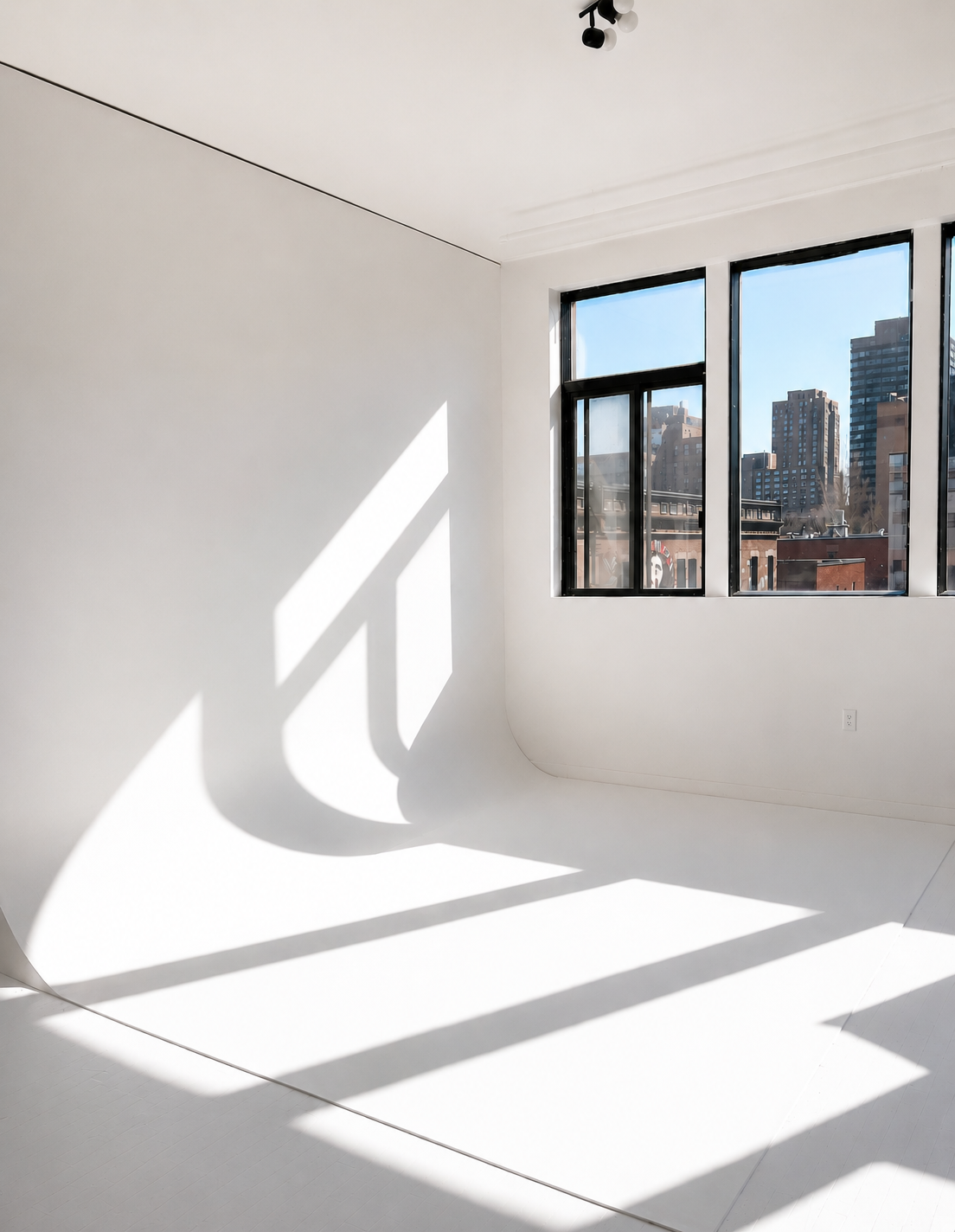Empty room with large windows casting shadows on cyclorama, city buildings visible outside.