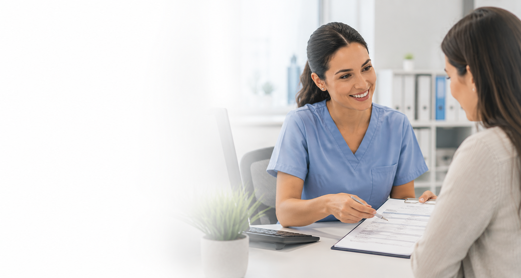 A nurse in blue scrubs smiling while consulting with a patient. The nurse holds a clipboard and pen, and the patient is sitting across from her in a medical office setting.