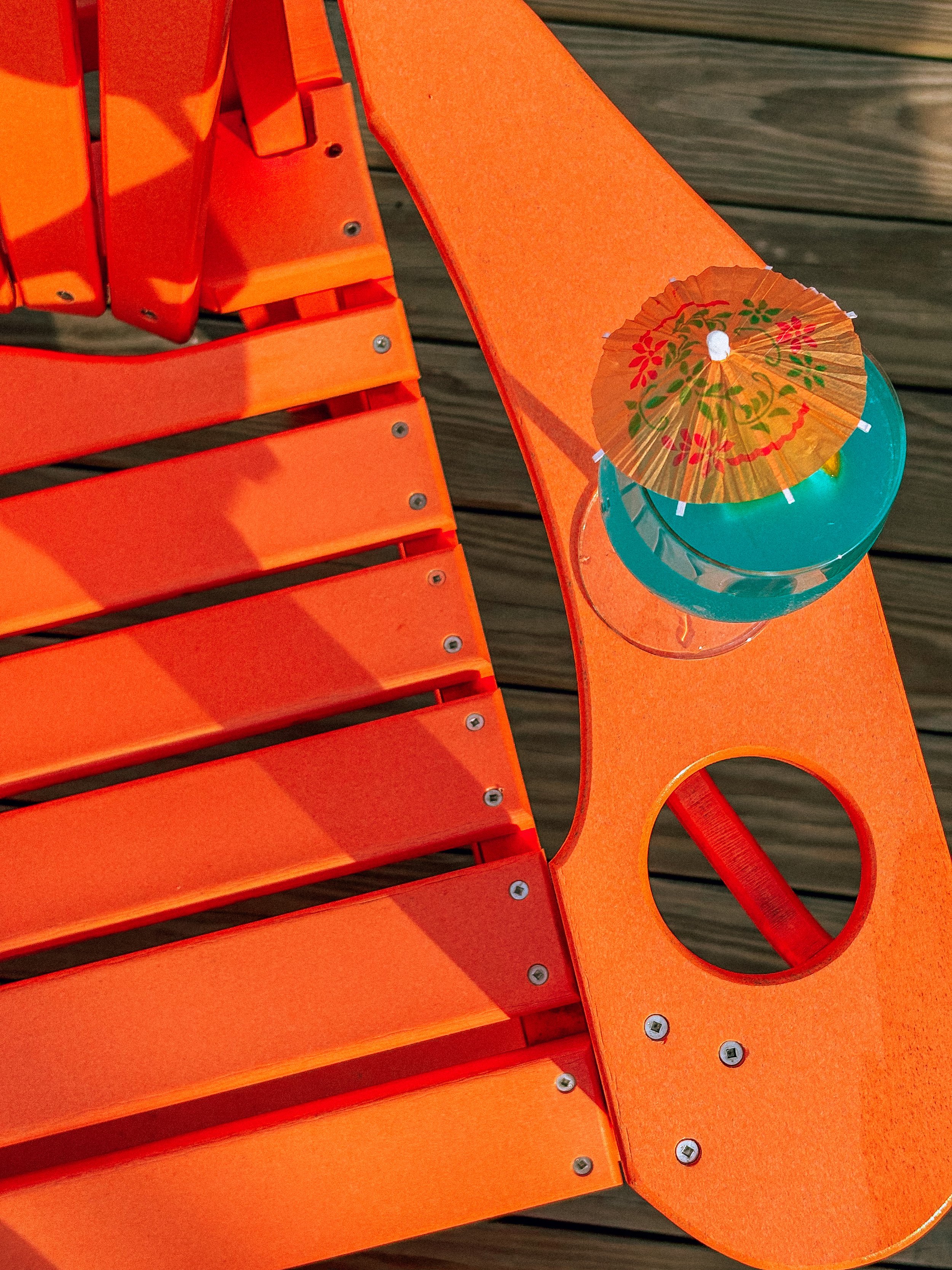 Orange outdoor lounge chair with a small table and a tropical drink with a paper umbrella on a wooden deck.
