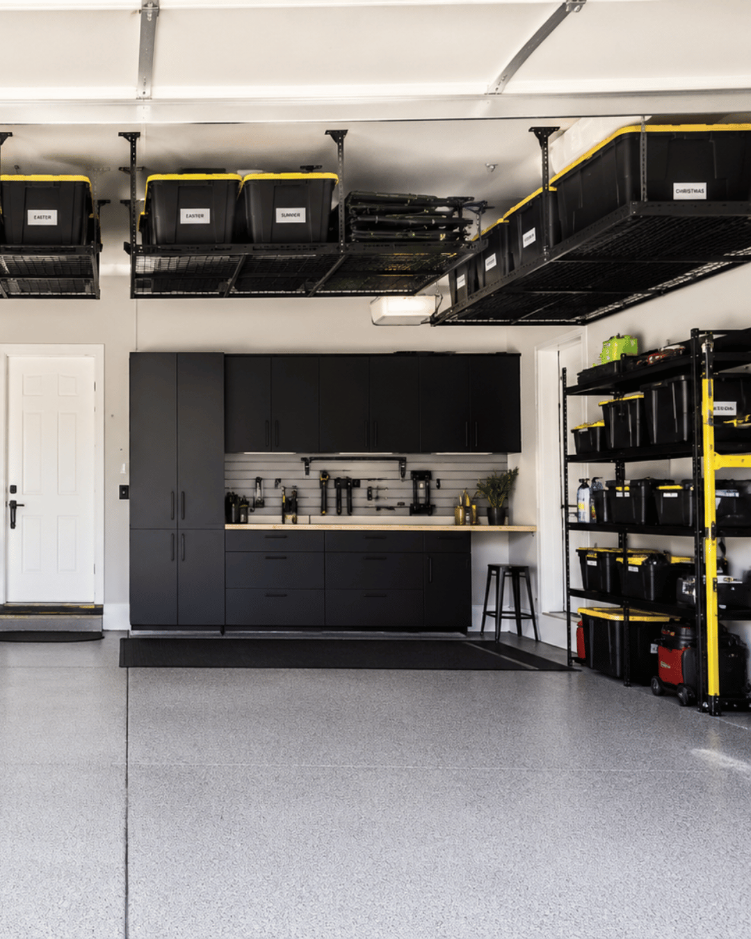 Organized garage with black cabinets, shelves of storage bins, and a workbench with tools and plants.
