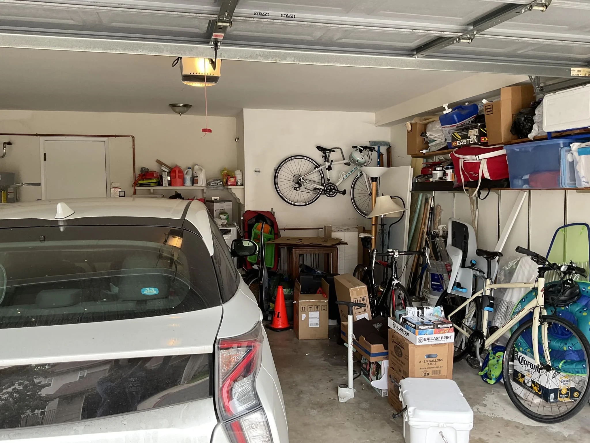 A cluttered garage containing various items including bikes, boxes, a car, and shelves with supplies.