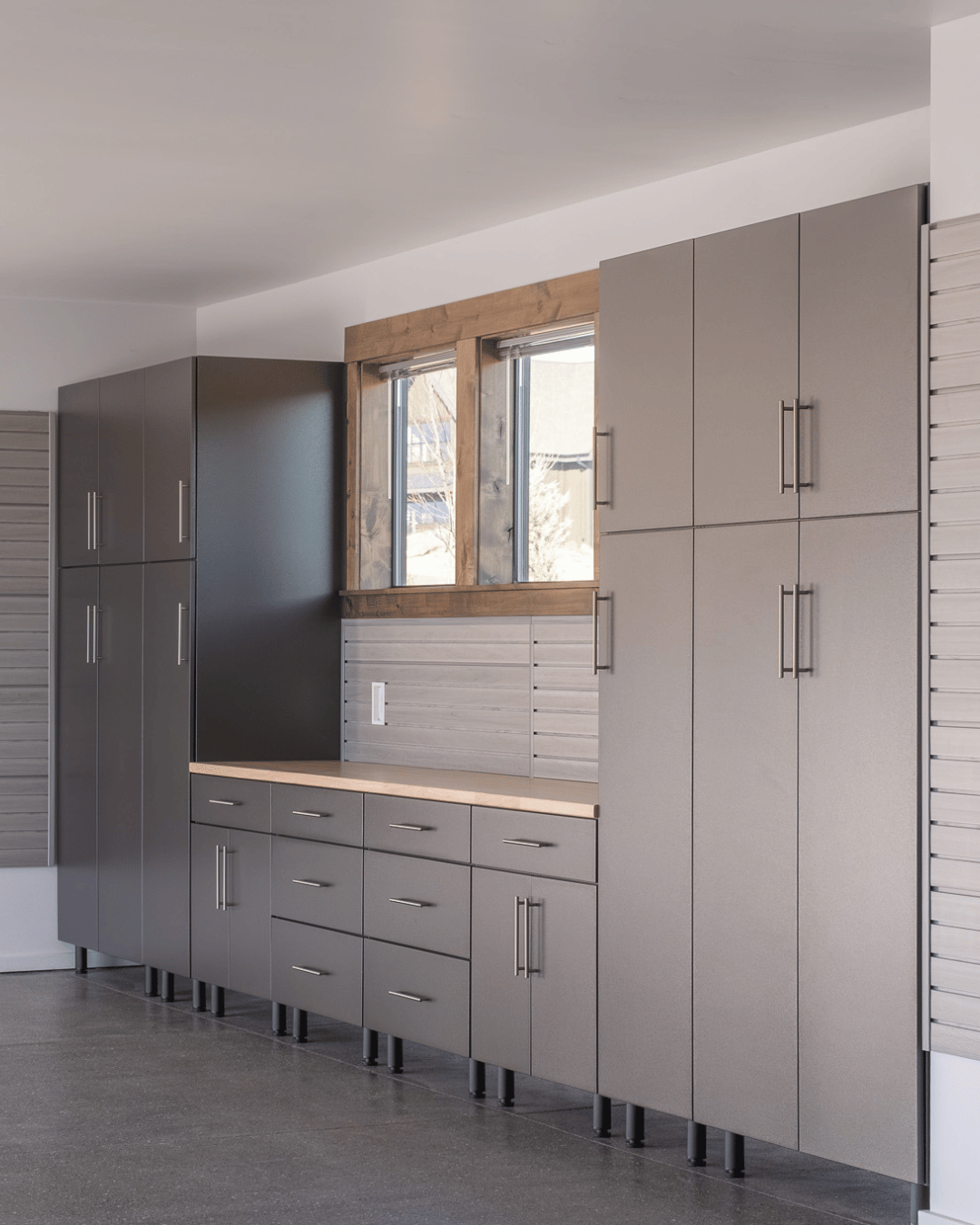 Modern kitchen with gray cabinets, wooden window frame, and a backsplash with horizontal paneling.