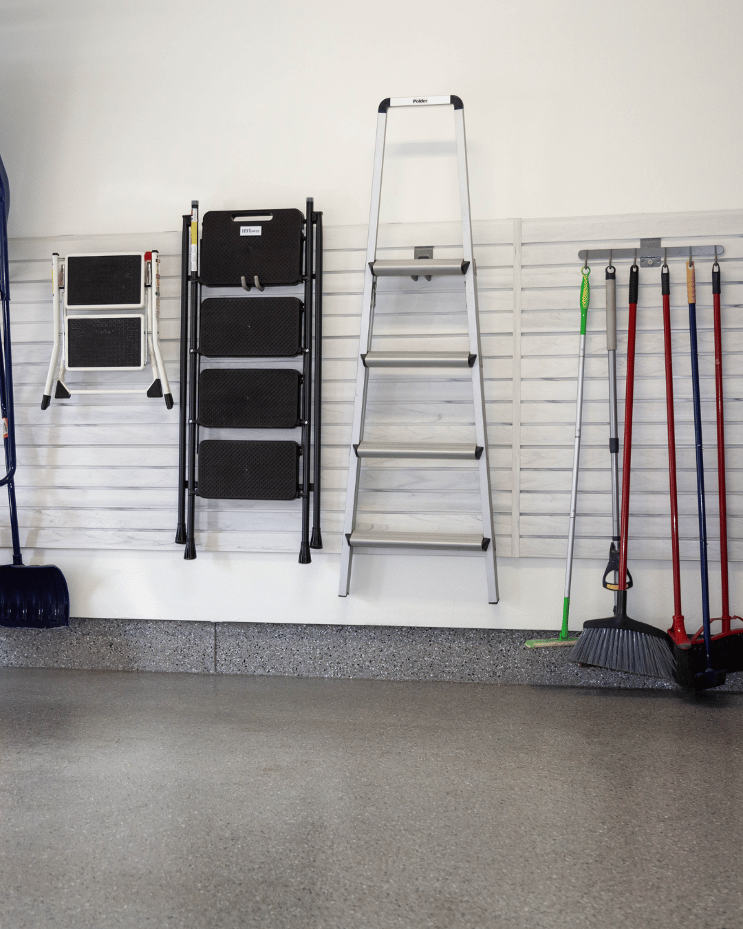 Garage wall with a ladder, step stool, and various cleaning tools hanging on hooks