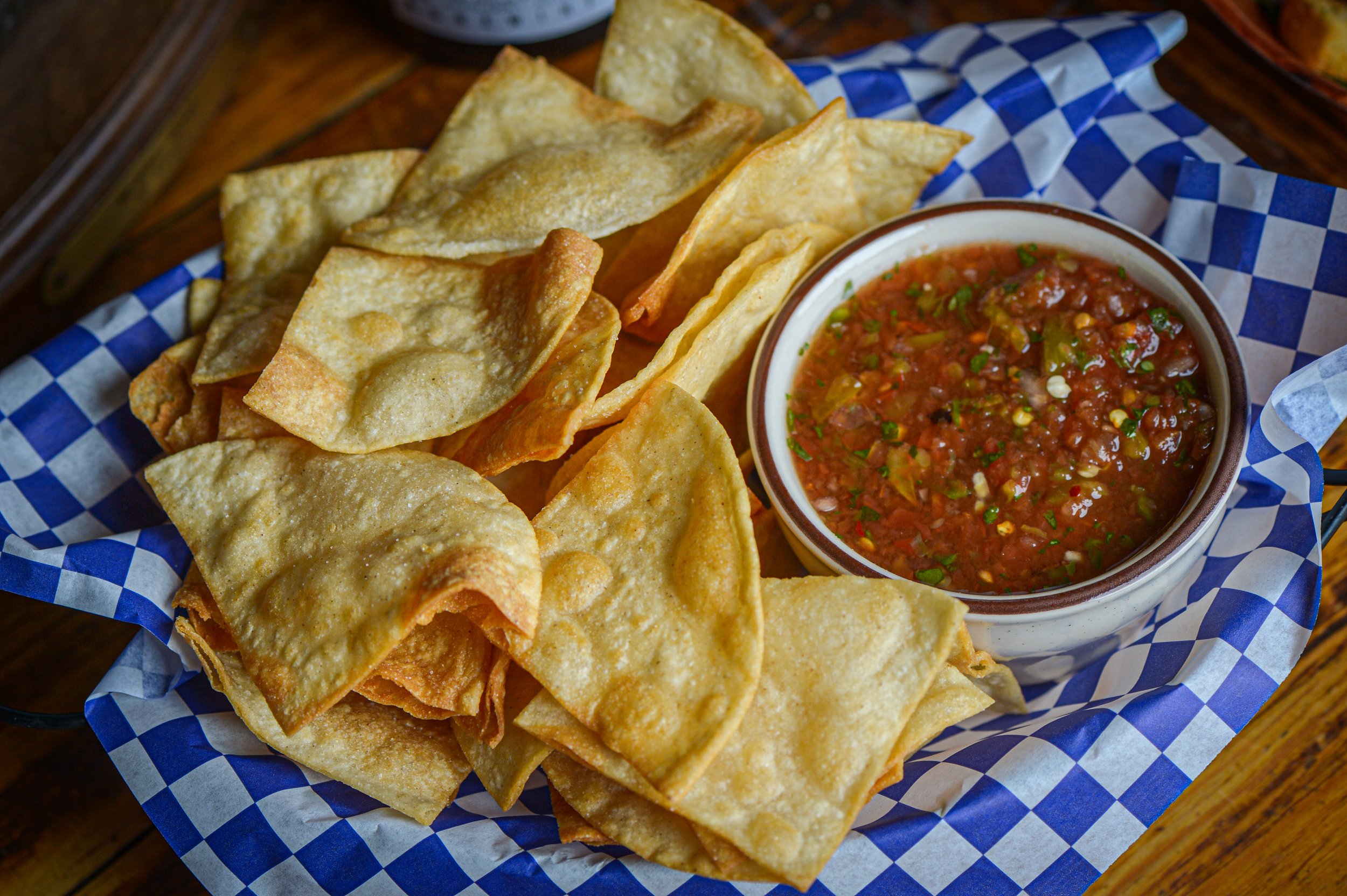 A basket of crispy tortilla chips with a bowl of salsa
