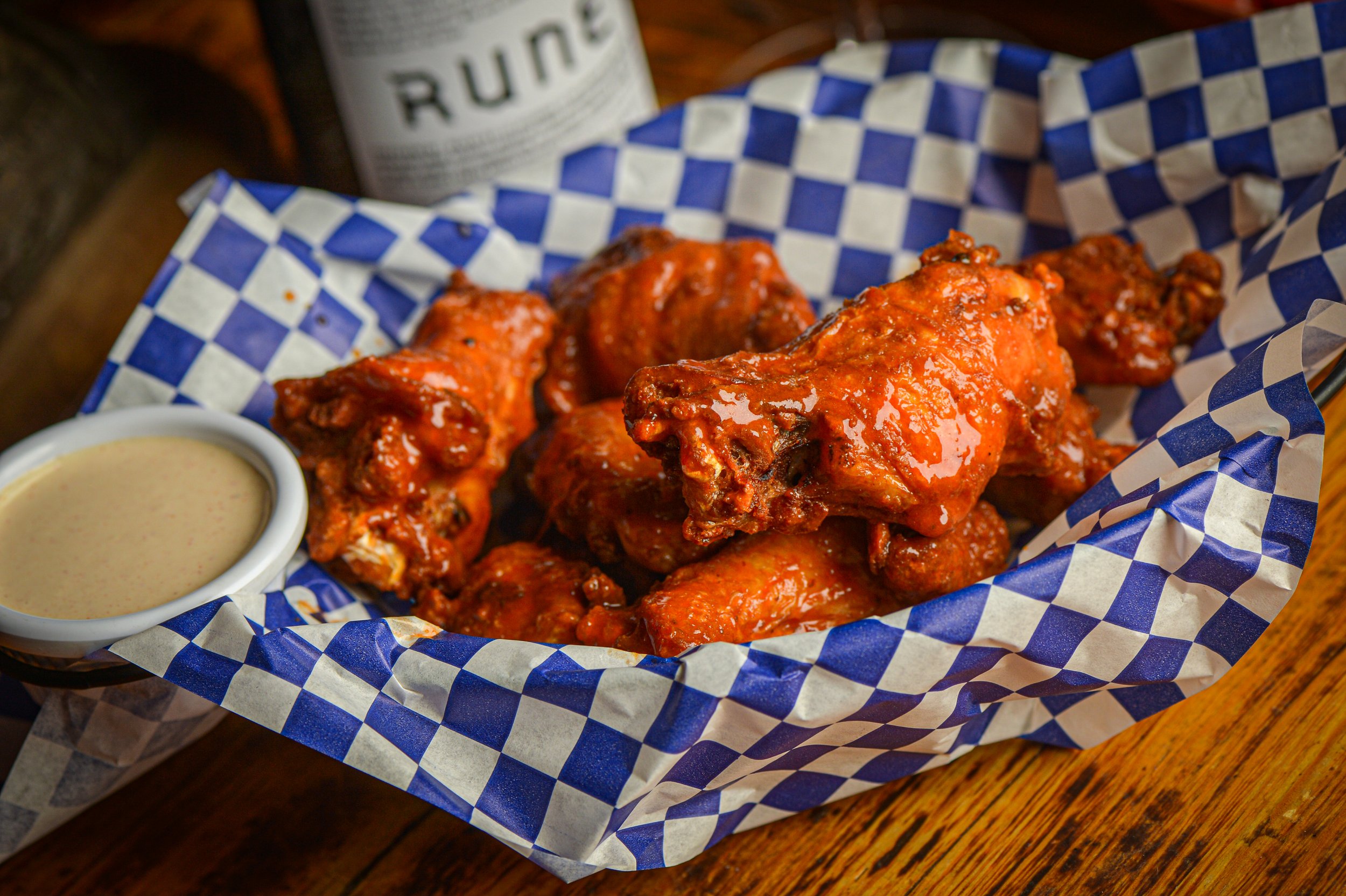 Basket of buffalo chicken wings with a side of dipping sauce on a wooden table.