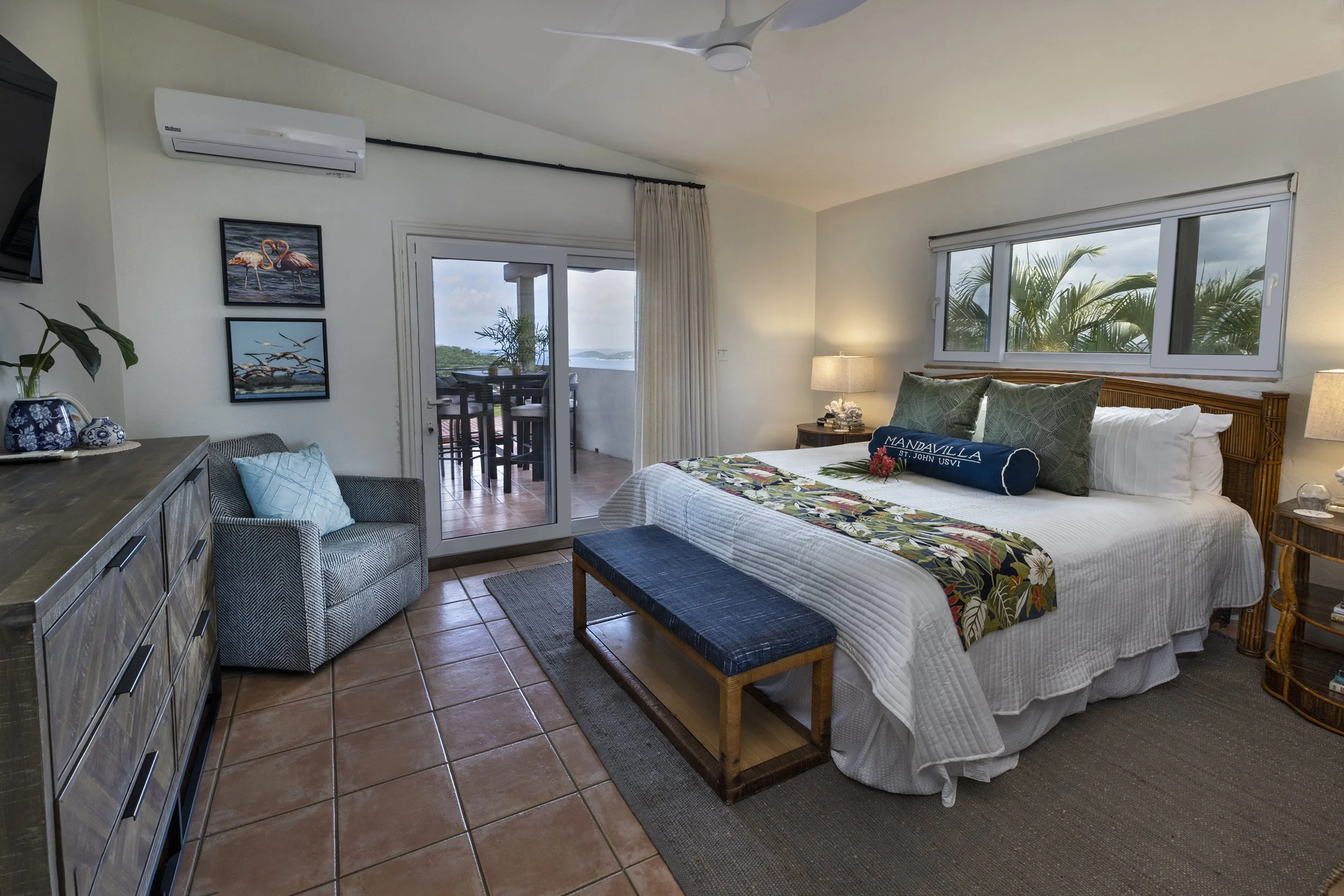 Mandavilla St. John USVI vacation rental A hotel room with a bed, nightstands, window, and balcony door, decorated with tropical-themed artwork and plants.