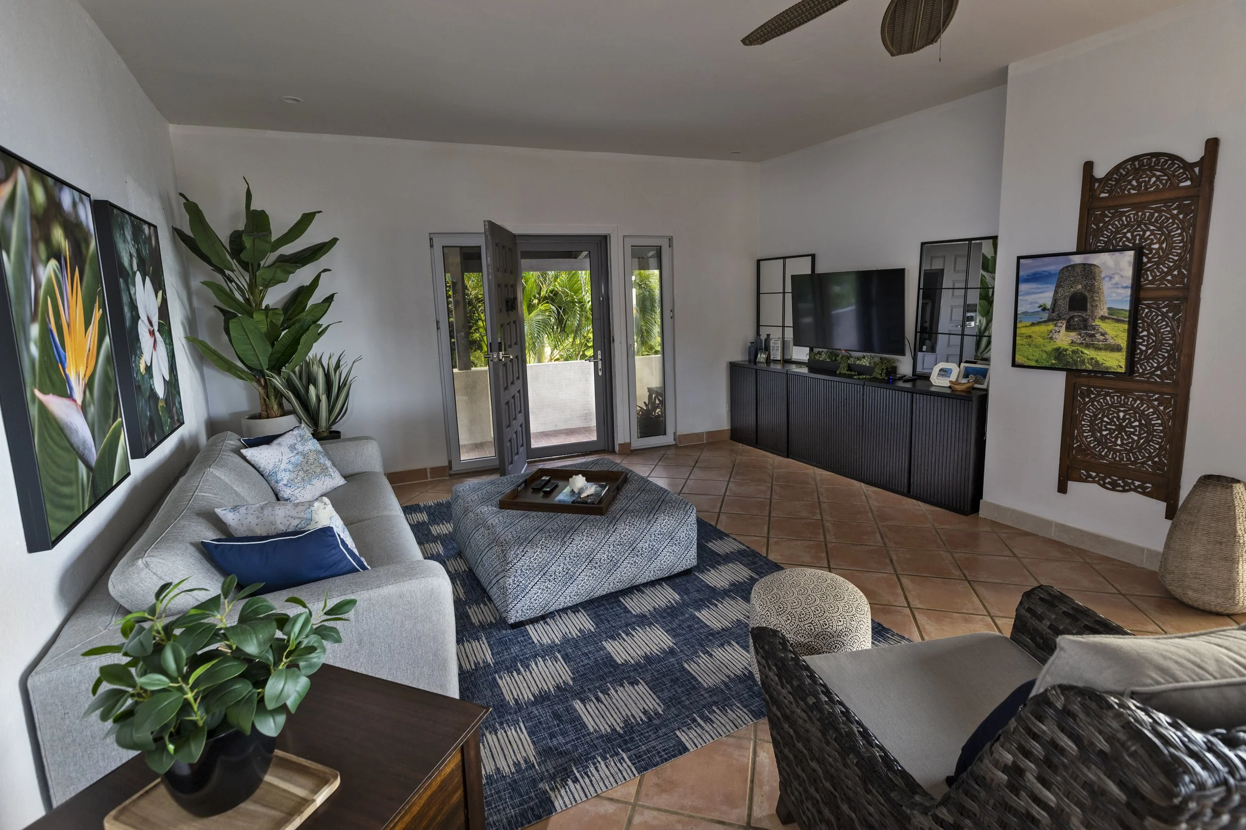 Mandavilla St. John USVI vacation rental Living room with a light-colored sofa, plants, wall art, a TV, and a door leading to outside greenery.