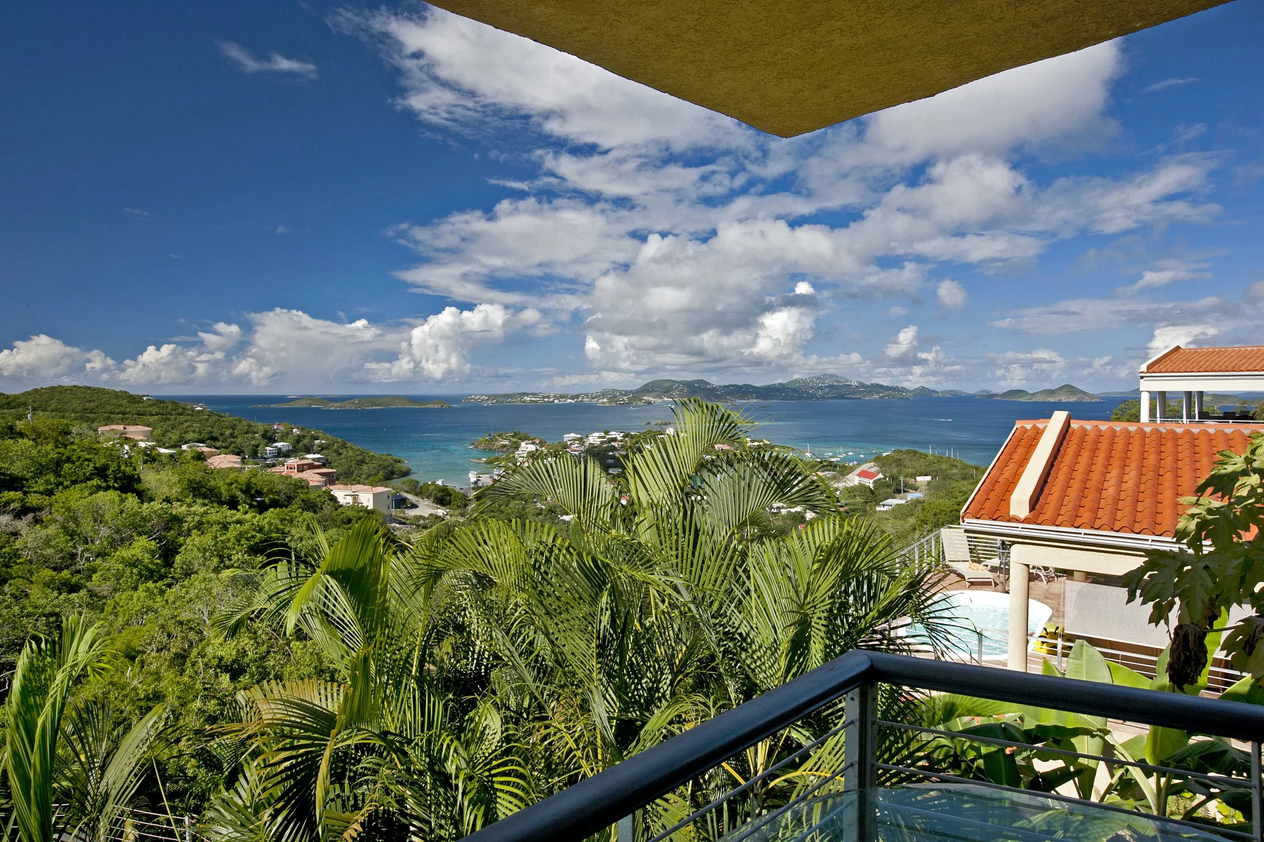 Mandavilla St. John USVI vacation rental Ocean view from a balcony with lush green trees, rooftops, and distant islands under a partly cloudy sky.