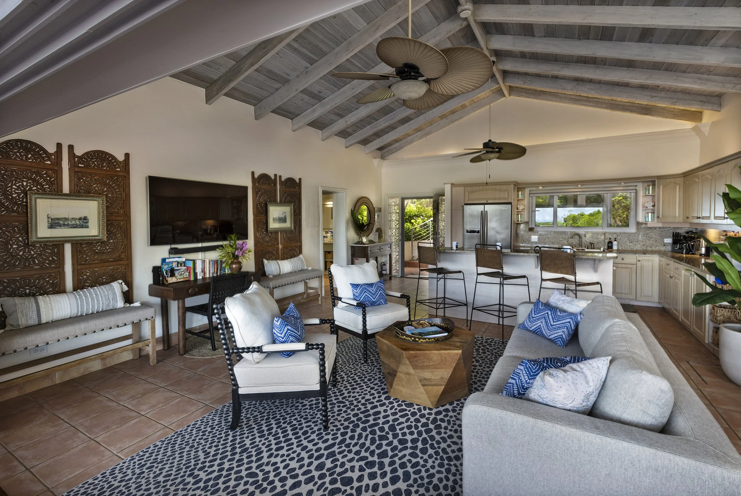 Mandavilla St. John USVI vacation rental Living room with white walls, wooden ceiling beams, ceiling fans, a large split-level kitchen with white cabinets, granite countertops, barstools, and large windows with an outdoor view.