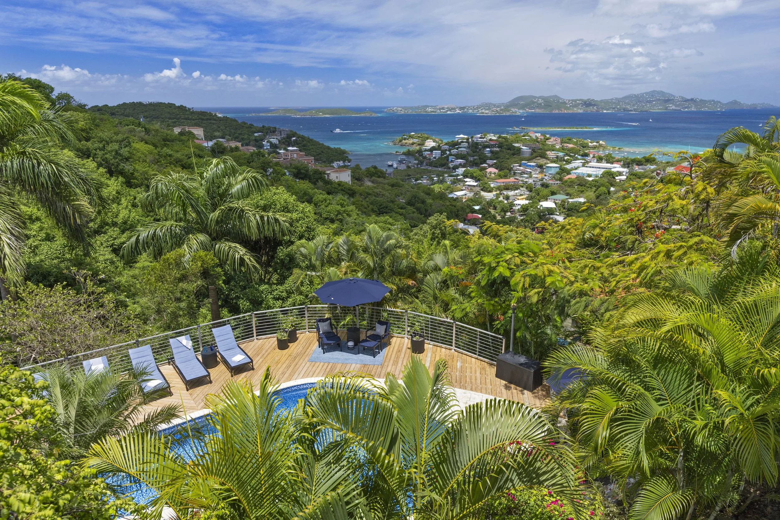 Mandavilla St. John USVI vacation rental  A view from a tropical hillside overlooking a coastal town with colorful buildings, lush greenery, and an expansive ocean with boats, islands, and hills in the distance.