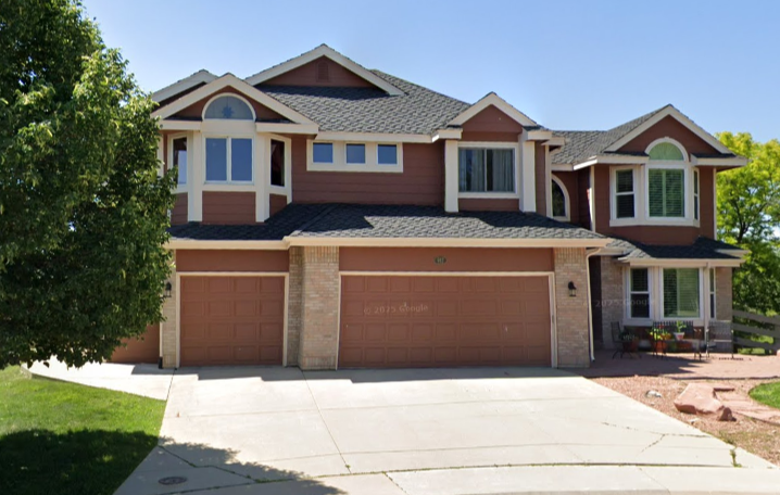 Front view of a two-story suburban house with a three-car garage, brick and siding exterior, and a landscaped yard with trees.