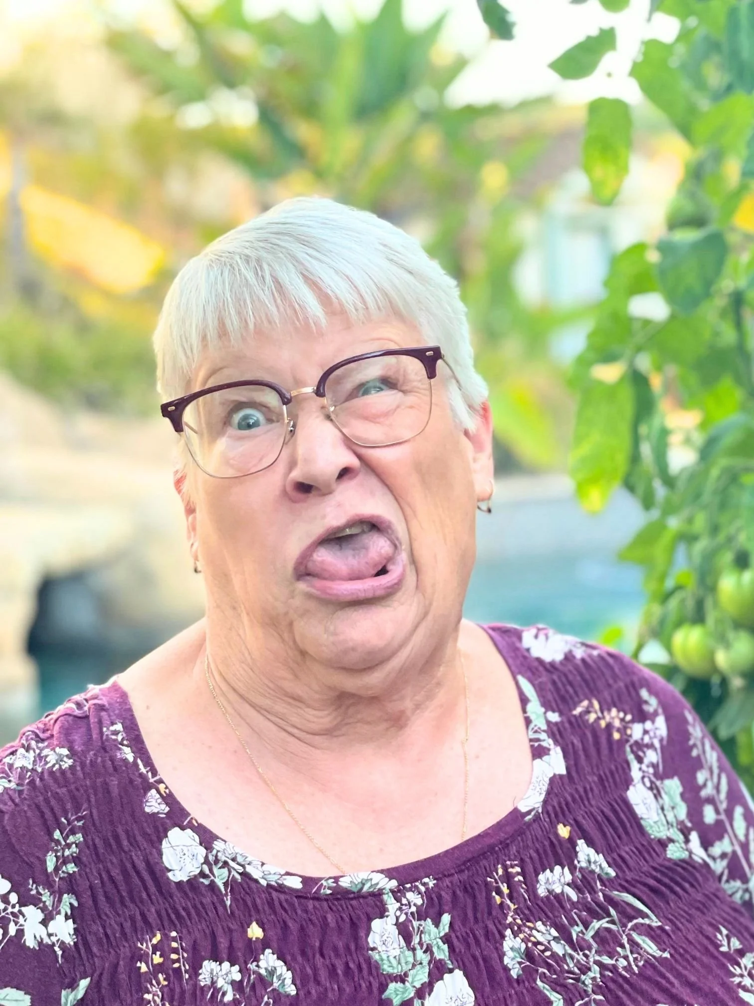 Close-up of Ms. Louise Thompson from LL Science Tutoring making a funny face, sticking out her tongue, outdoors with green foliage in the background.