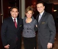 Three people dressed in formal attire standing together and smiling for the photo.