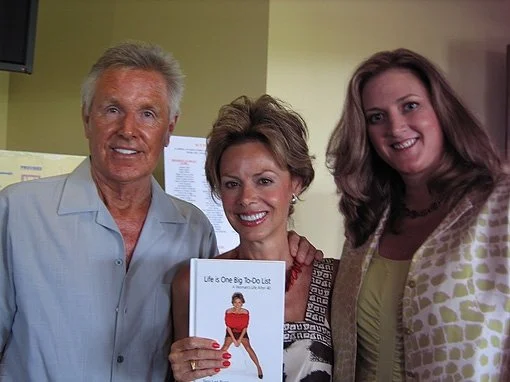 Three people smiling and holding a book titled "Life is One Big To-Do List" in an indoor setting.