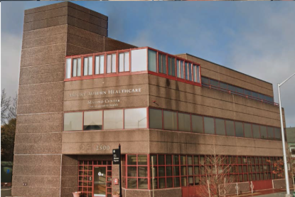 A multi-story beige building with red window frames and a red trim at the top, labeled 'Northern Healthcare' and 'Radio City', with a street sign and some trees in front.