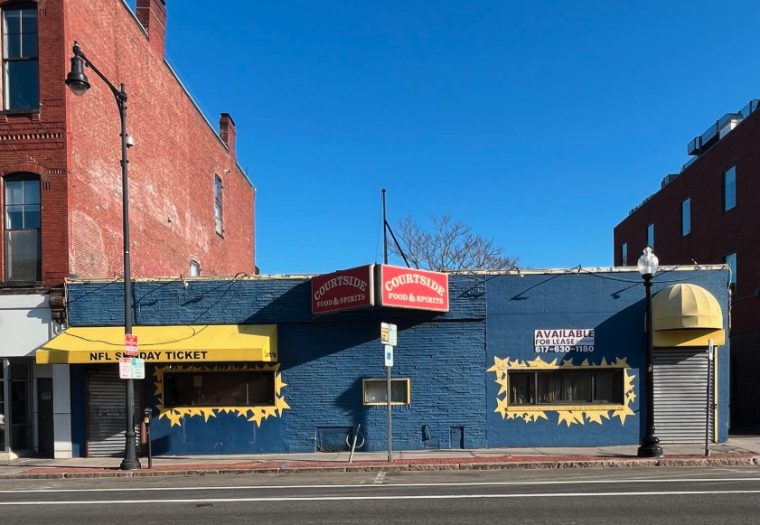 Blue building with CVS sign, yellow awning, two windows decorated with yellow stars, and a yellow dome-shaped awning on the right side. A sign on the left mentions NFL Sunday Ticket, and a sign on the right indicates availability for lease. Two tall 