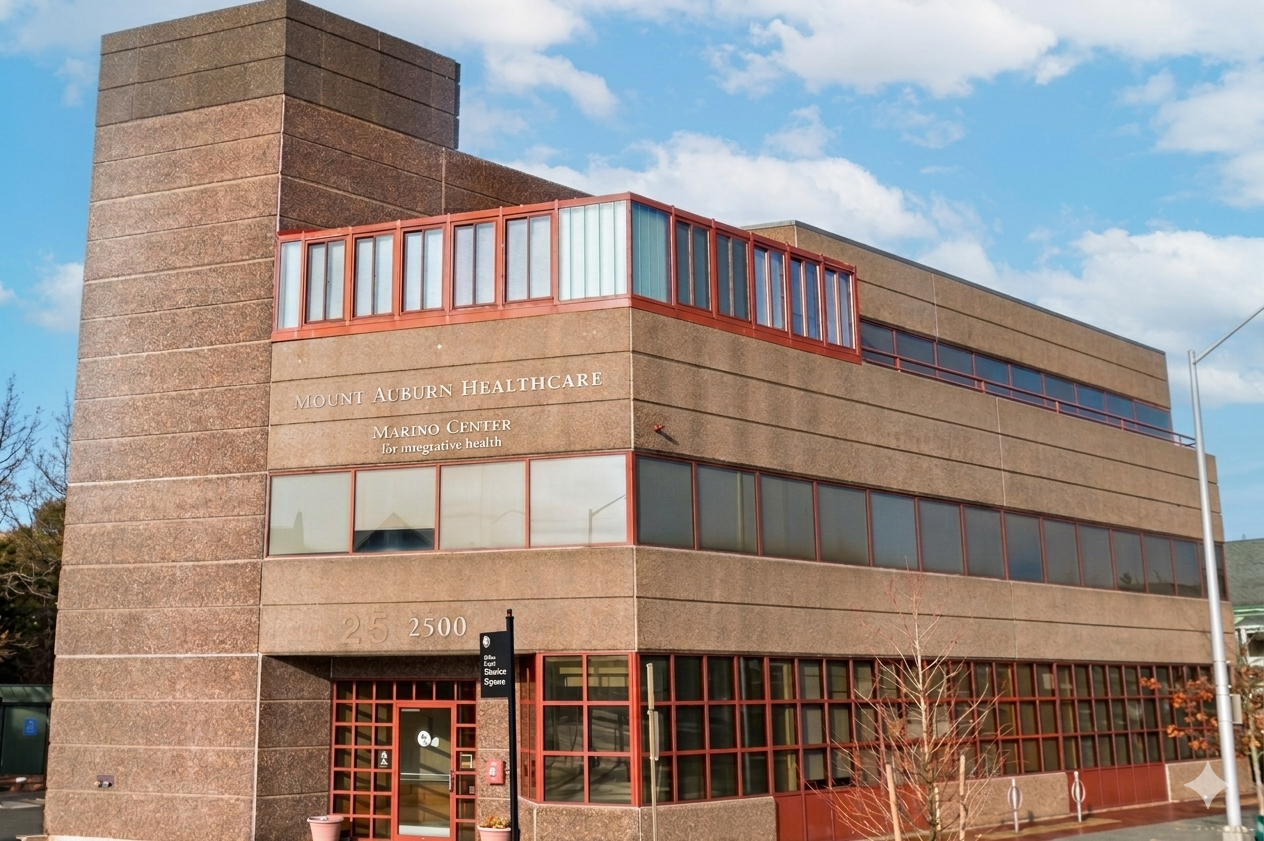 Exterior of Mount Auburn Healthcare Marino Center building with large windows and brick facade under a partly cloudy sky.