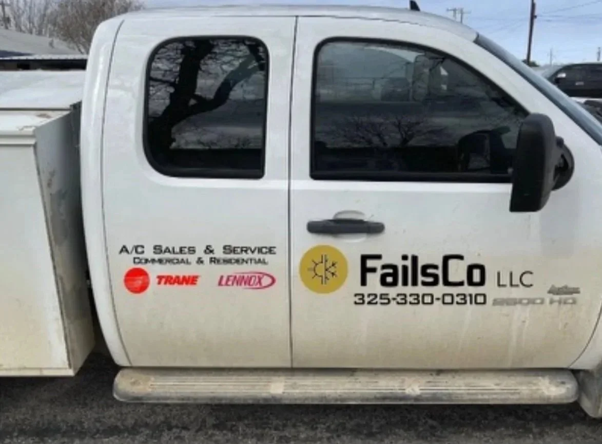 Side view of a white utility truck with company logos and contact information, parked outdoors.