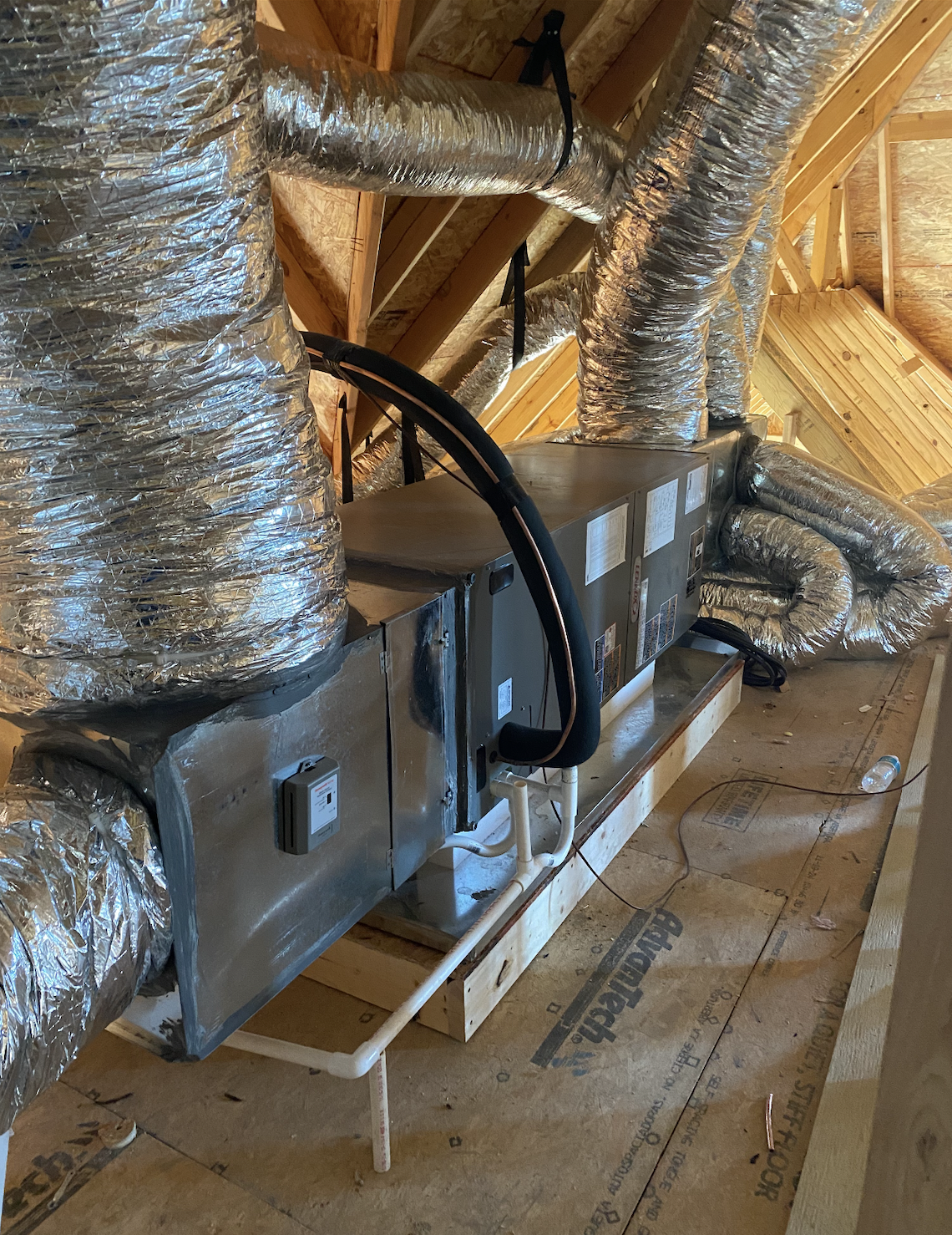 View of HVAC ductwork and equipment installed in the attic of a house under construction, with wooden framing and exposed insulation.
