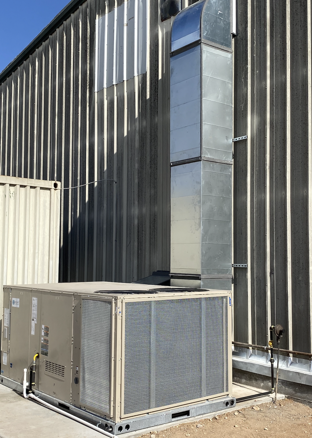 An industrial HVAC unit installed next to a corrugated metal building with a vertical duct attached to the wall.