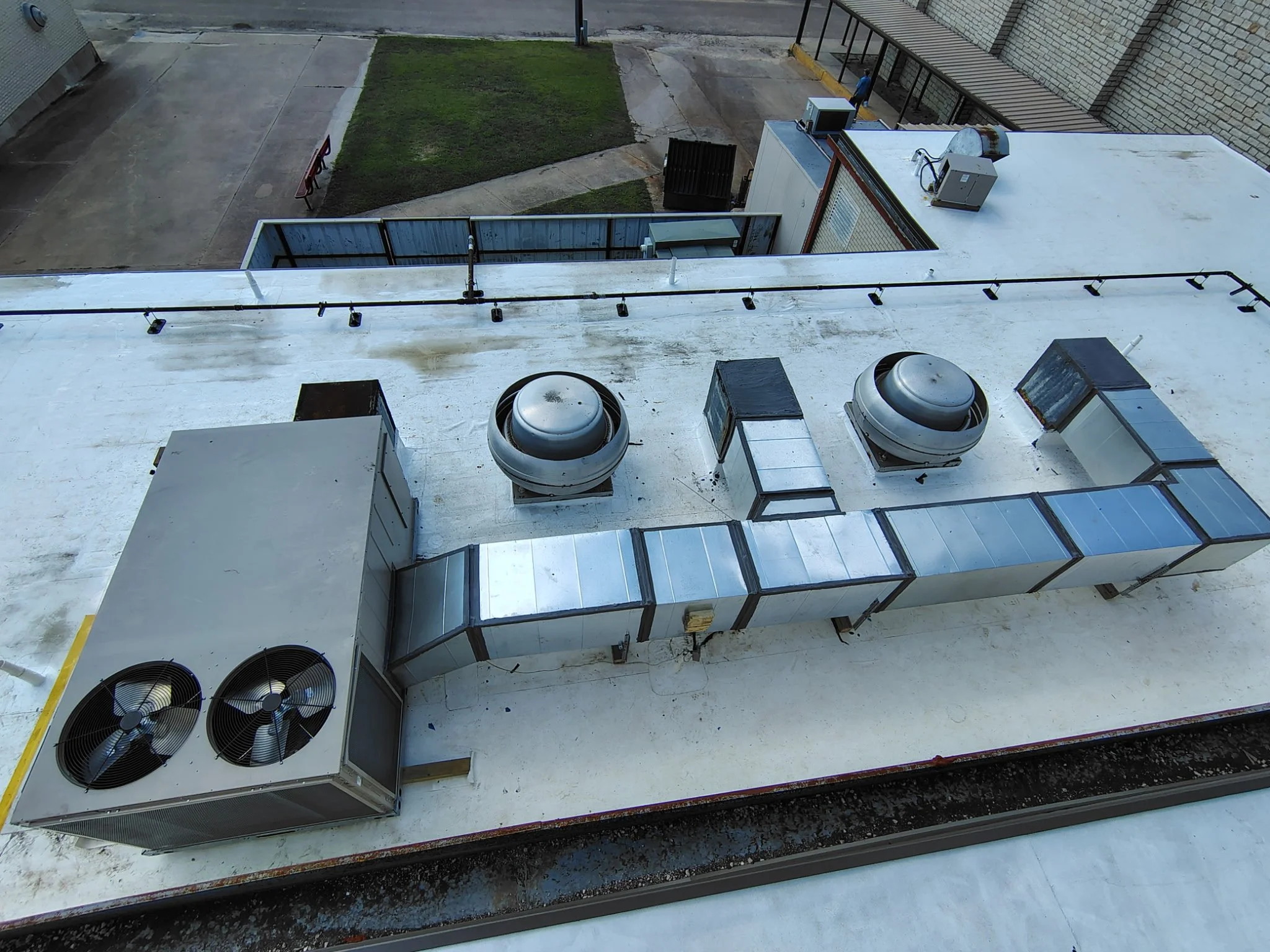 View of rooftop HVAC units and ventilation systems on a building, with some exhaust fans visible and a flat white roof surface.