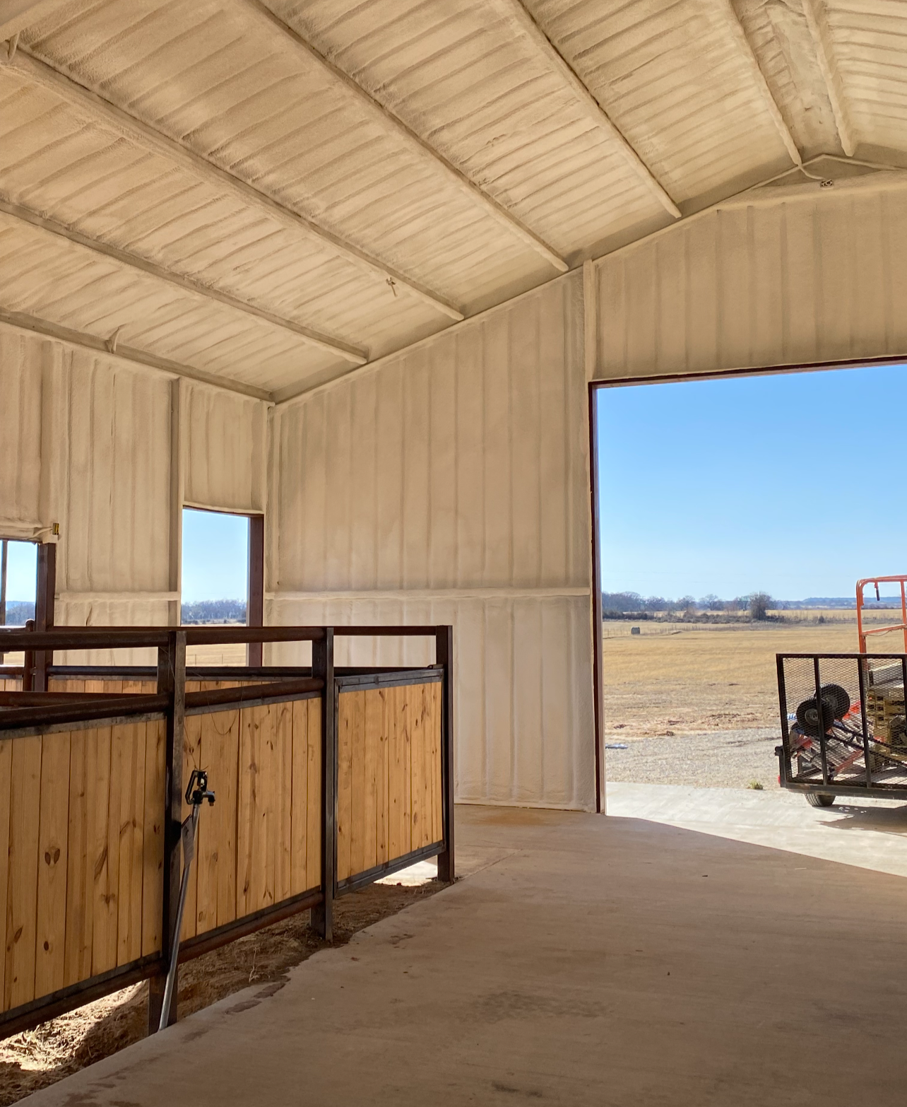 Inside view of a barn under construction with unfinished wooden walls, large open doorway, and farm field visible outside.