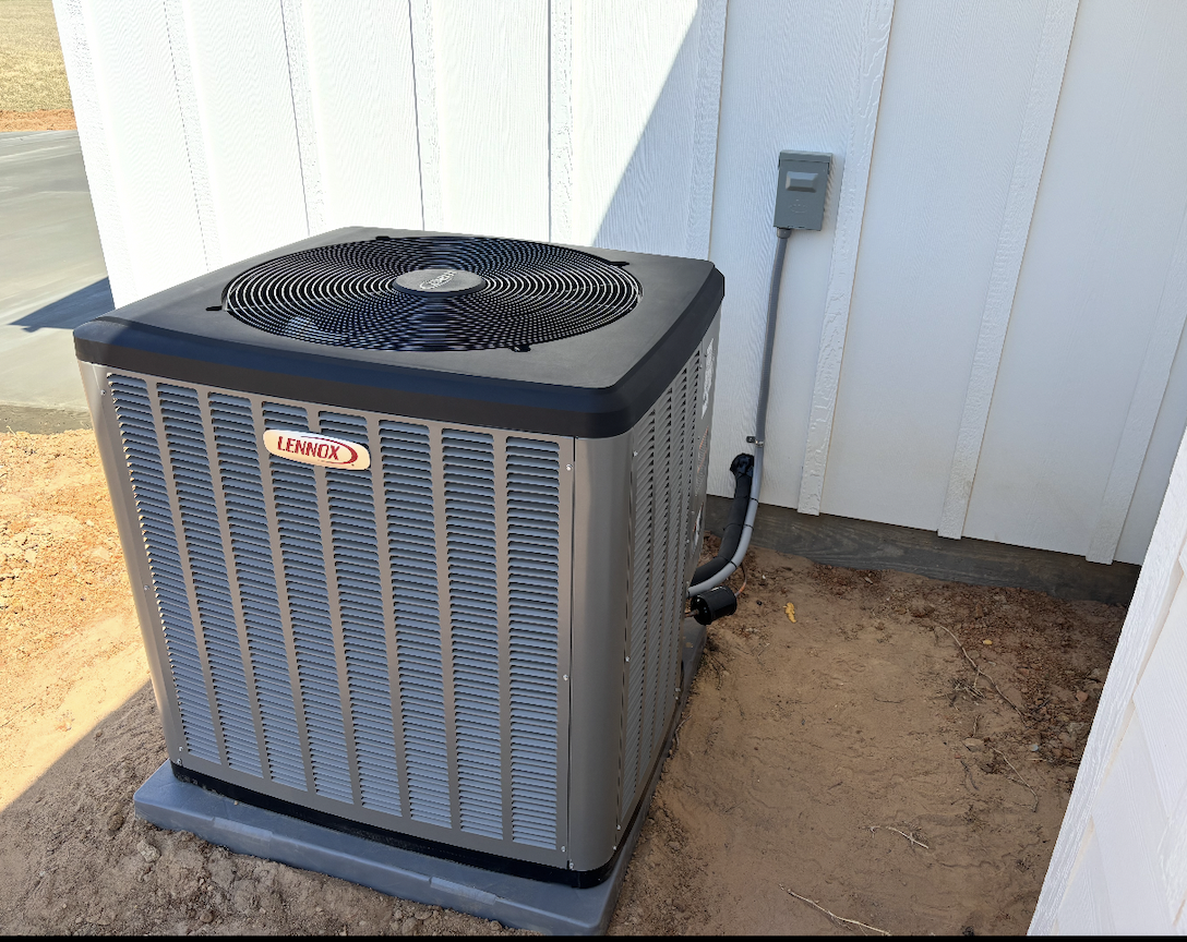 Outdoor Lennox air conditioning unit next to a white exterior wall, with electrical wiring connected and resting on a concrete pad.