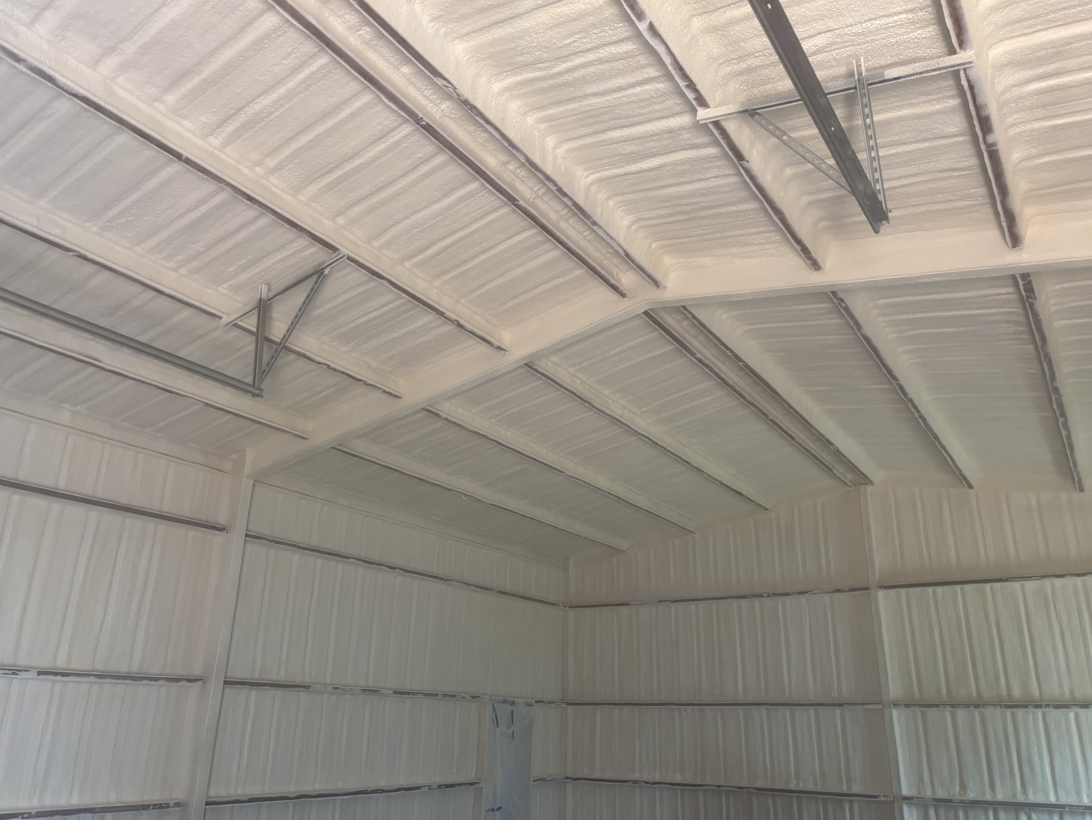 The ceiling of a large industrial or commercial building, showing metal beams and spray foam insulation.