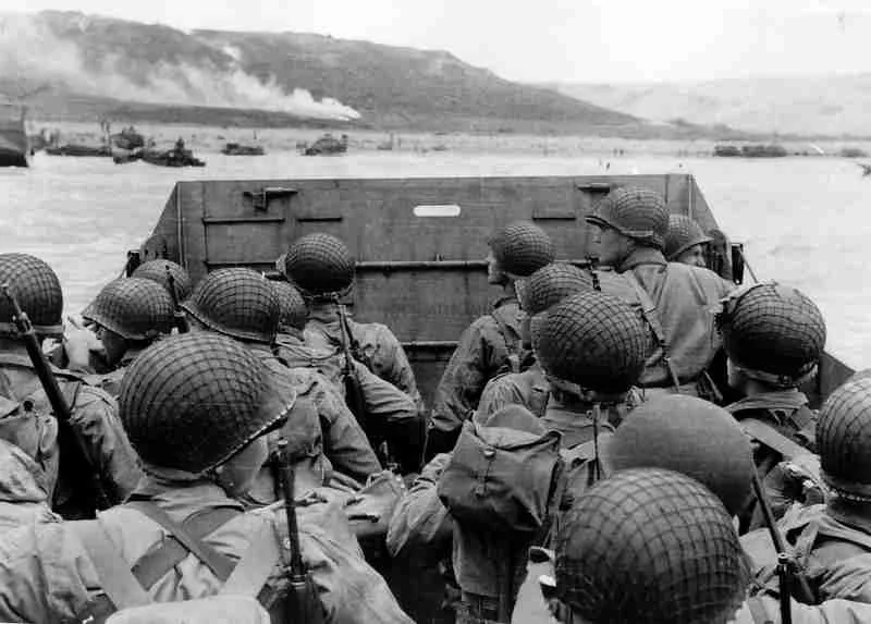 Military soldiers wearing helmets and gear aboard a boat on a river during a historical military operation in black and white.