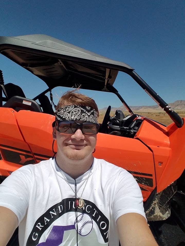 A man taking a selfie in front of an orange off-road vehicle in a desert landscape.