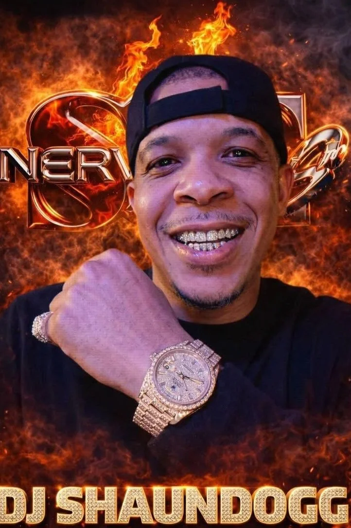 A man smiling, wearing a black cap and large diamond-encrusted watch, with a fiery background and the words 'ENERGY' and 'DJ SHAUNDOGG' in bold text.