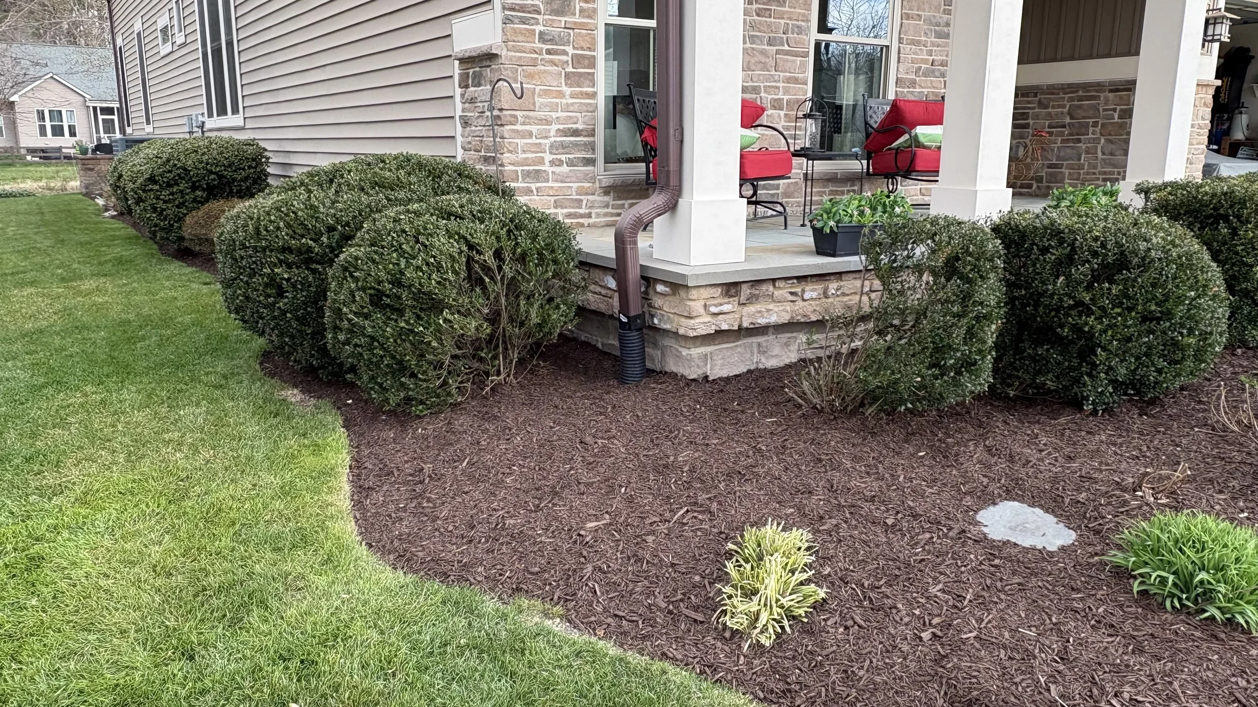 A landscaped front porch with bushes and mulch, a stone foundation, and red cushioned chairs on the porch  in Frankford, Delaware..