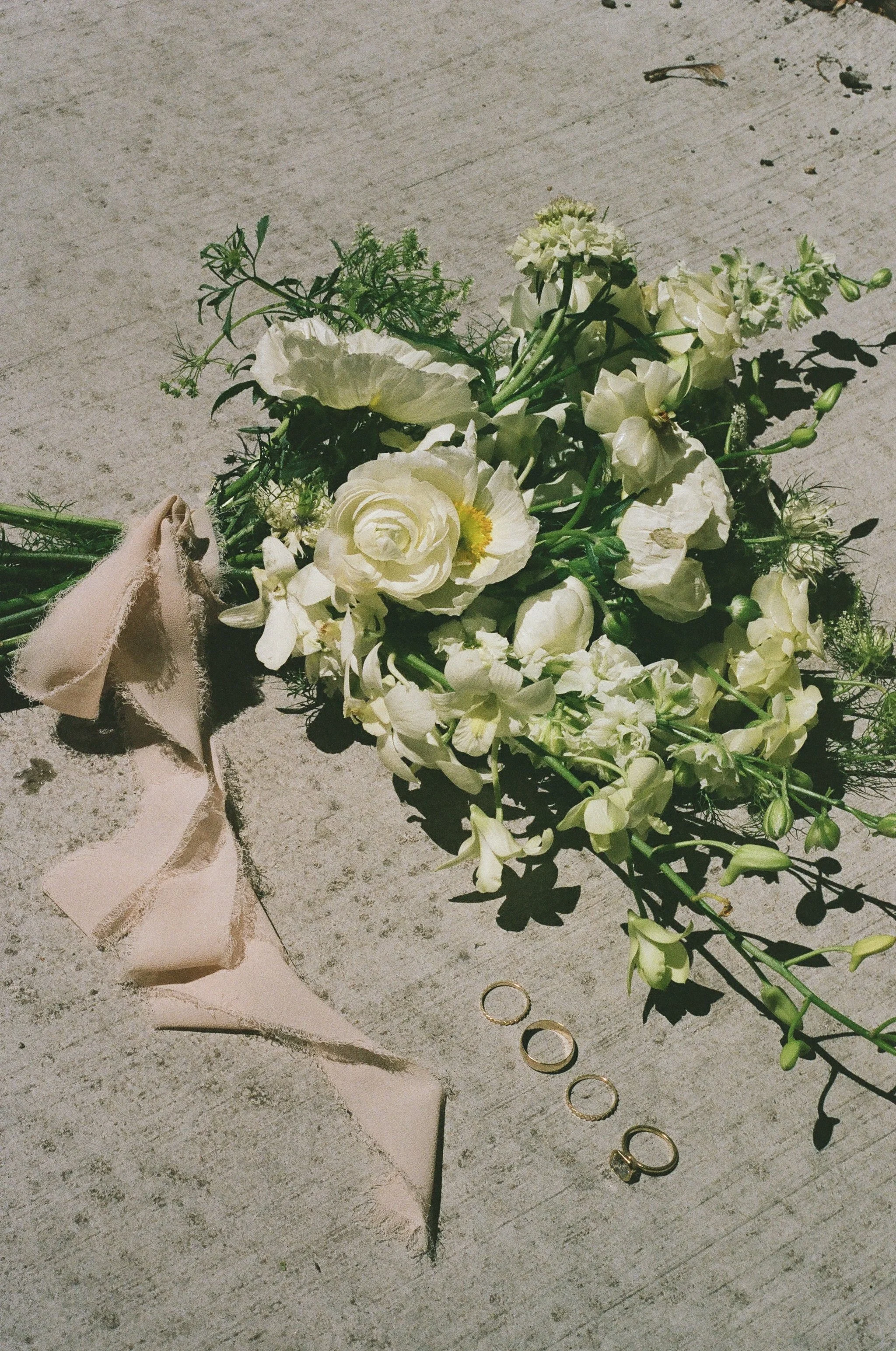 A bouquet of white flowers, ribbon, and wedding rings on a wooden surface.