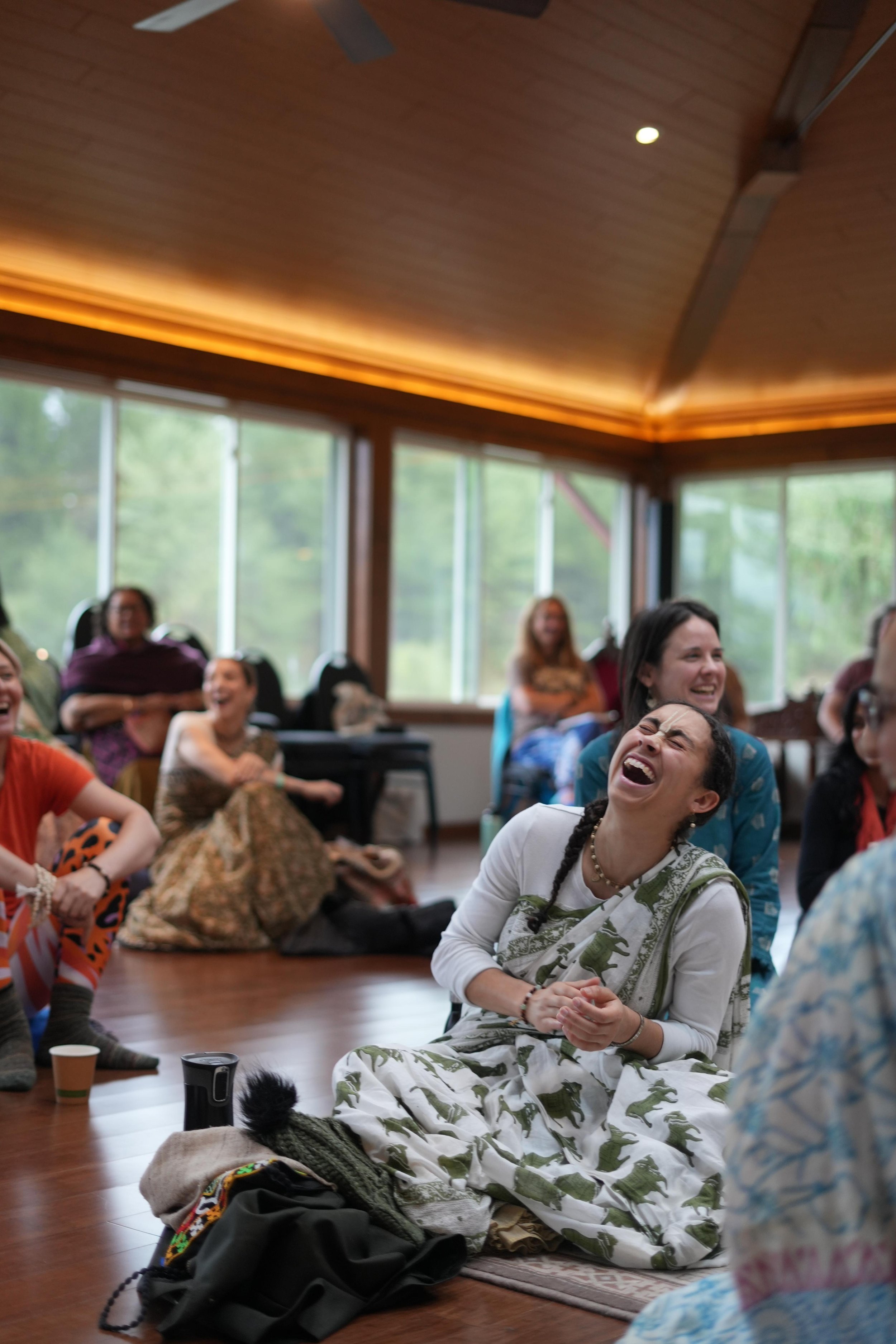 People sitting on the floor and laughing in a cozy room with large windows and wooden ceiling.