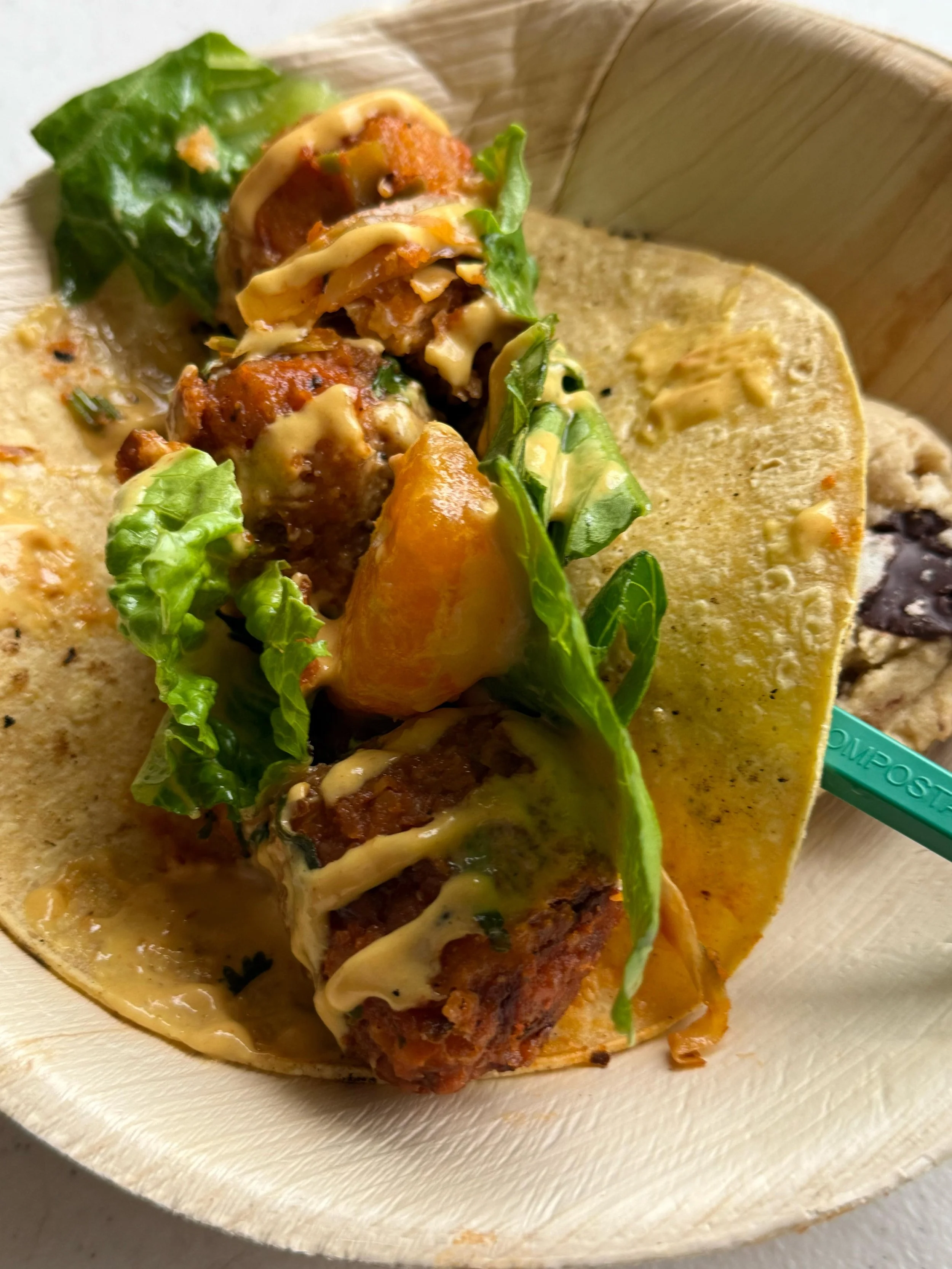 Close-up of a taco with lettuce, meat, cheese, and sauce in a wooden bowl.